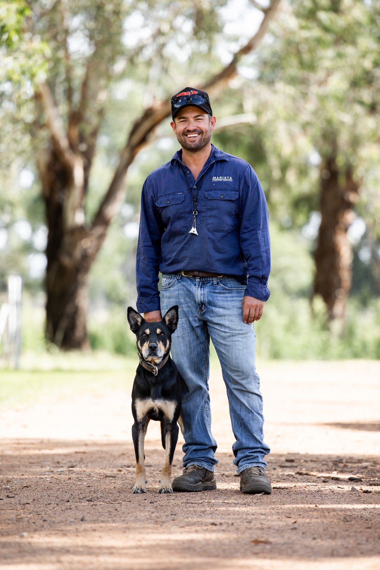 Livestock contractor with his black and tan kelpie dog standing on a road in a rural setting