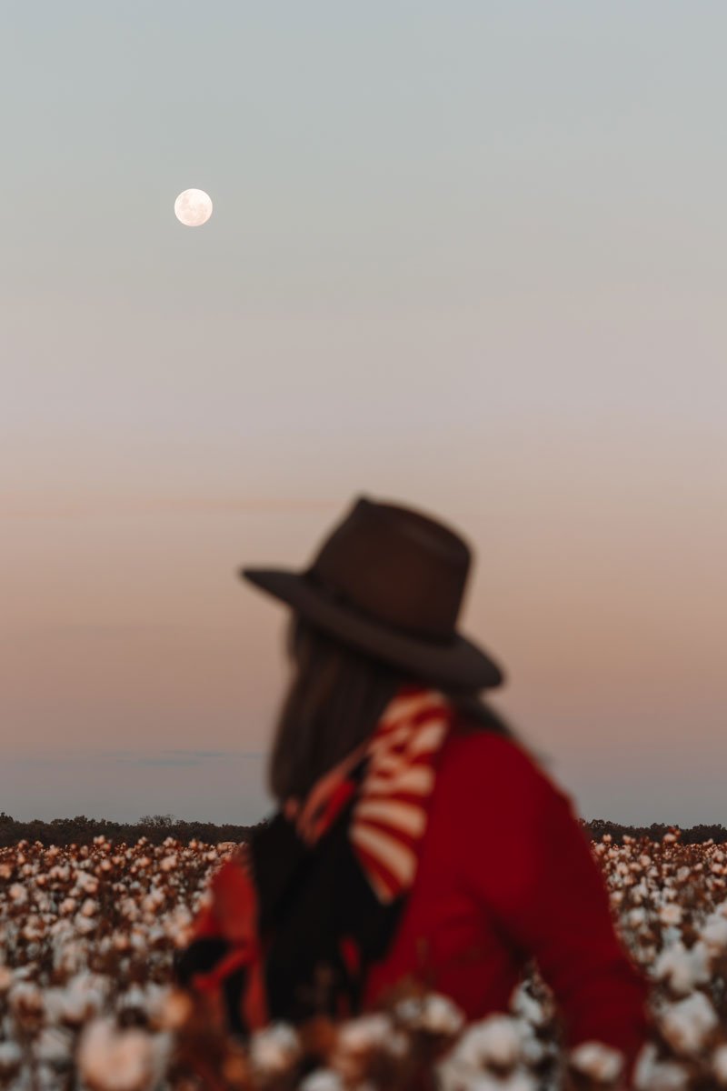 Woman in a cotton field wearing akubra hat with moon in the background