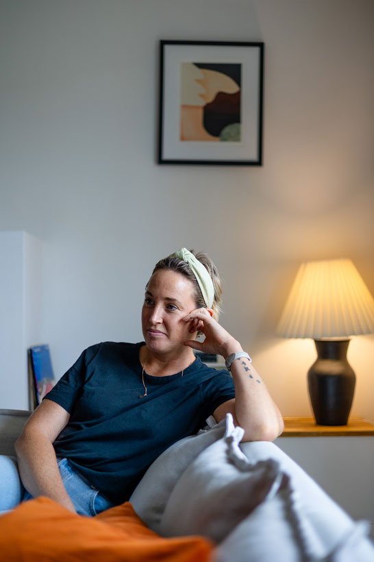 Woman sitting on a couch in a relaxed pose with a lamp on in the background