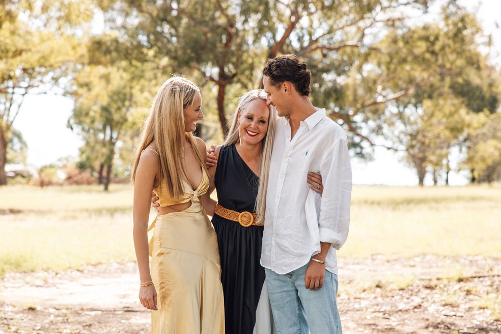 Two teenage children with their single mum hugging and smiling in a park