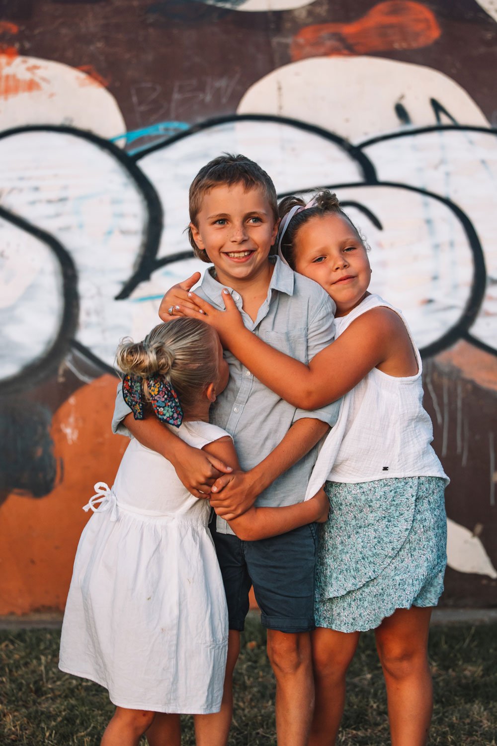 Three young sibling children cuddling with graffiti in the background