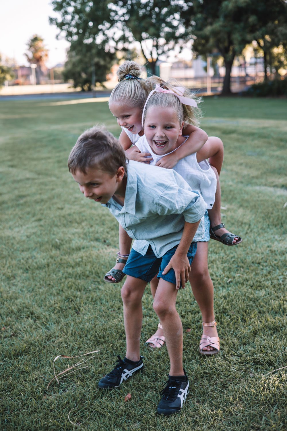 Three young sibling children playing and laughing in a park