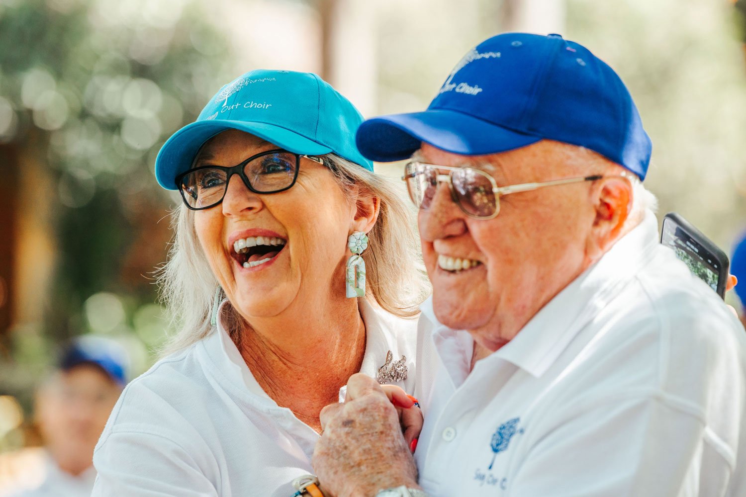 Close up of an older couple holding hands, laughing and dancing with bright blue caps on