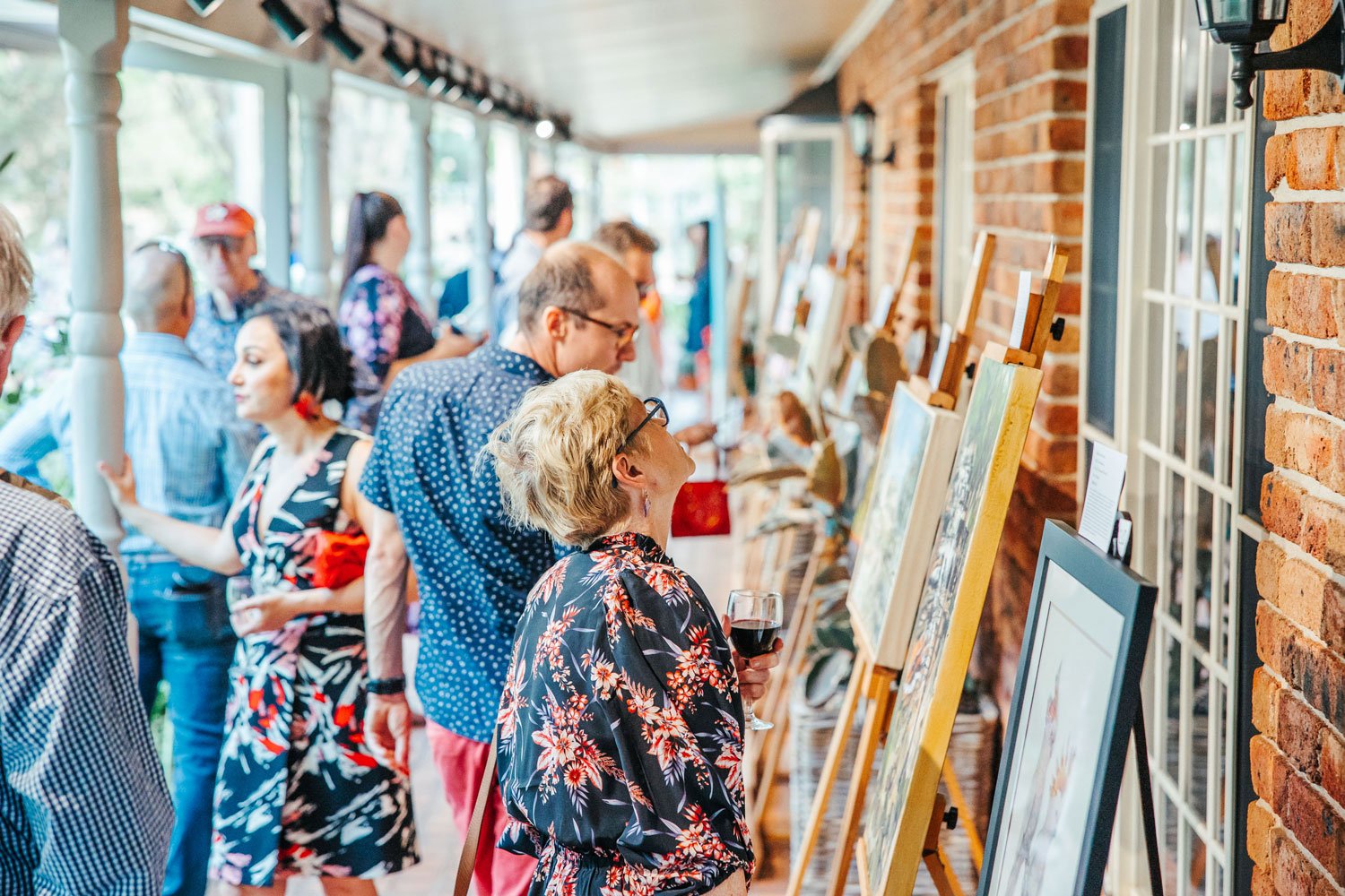 People looking at artwork in an open art exhibition on a verandah