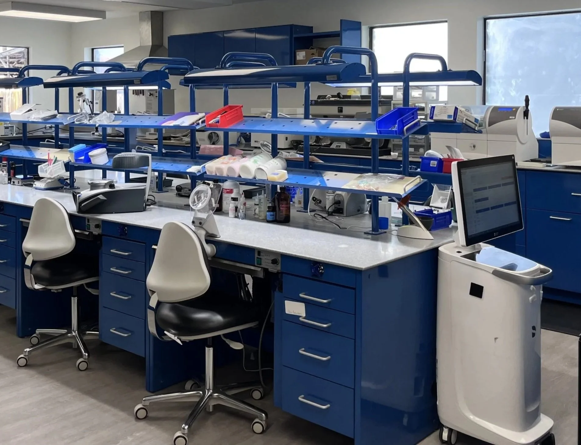 Medical laboratory with blue workstations, chairs, and equipment for testing and specimen processing.