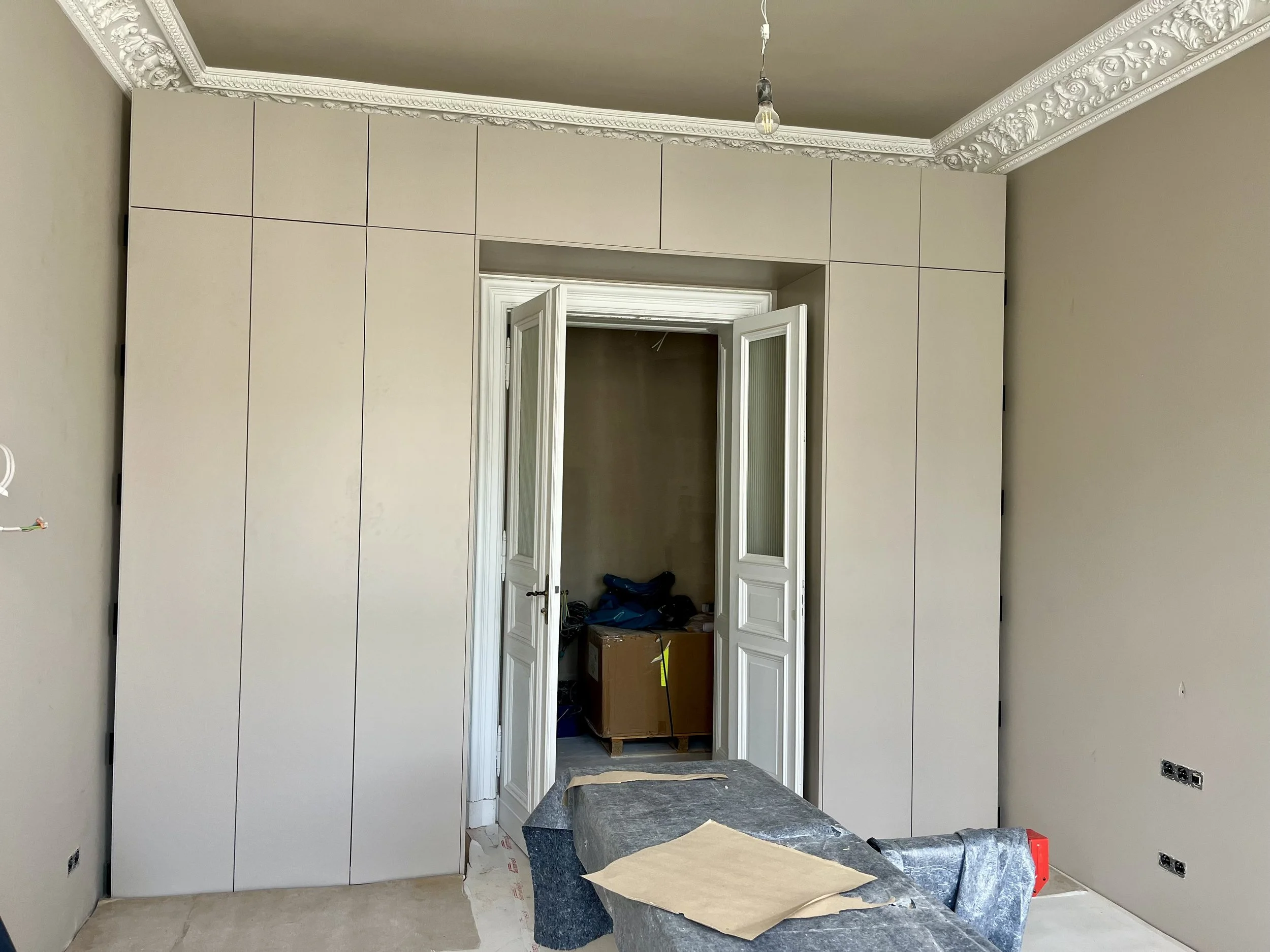 Innenraum eines Zimmers mit frisch installierter Wandverkleidung, eine offene Tür, sichtbarer Deckenleiste und Kabelauslass, Bauarbeiten sind im Gange.