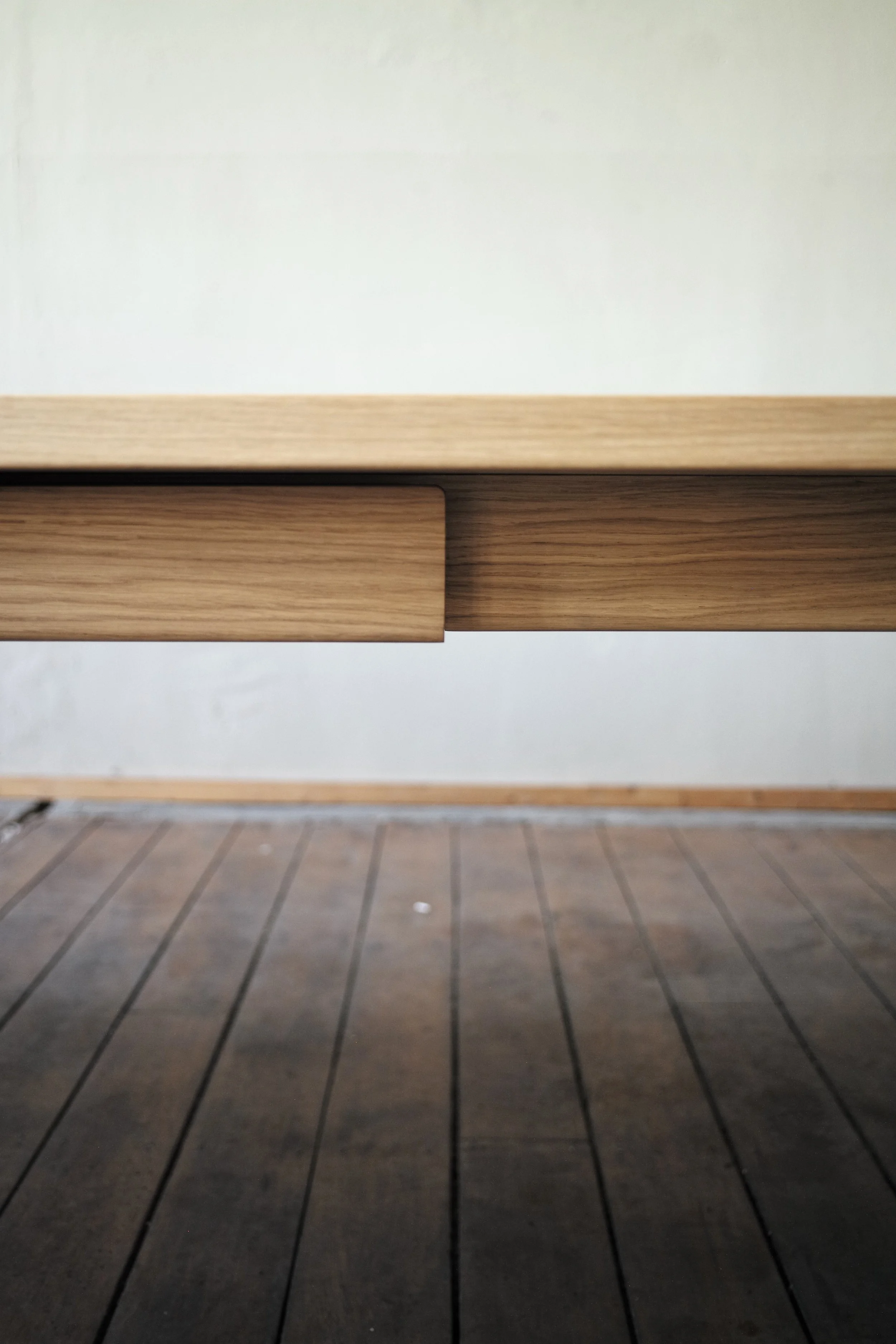 Nahaufnahme eines Holzregals oder -tisches mit einem geschlossenen Schubladen und einer dunklen Holzbodenfläche darunter.