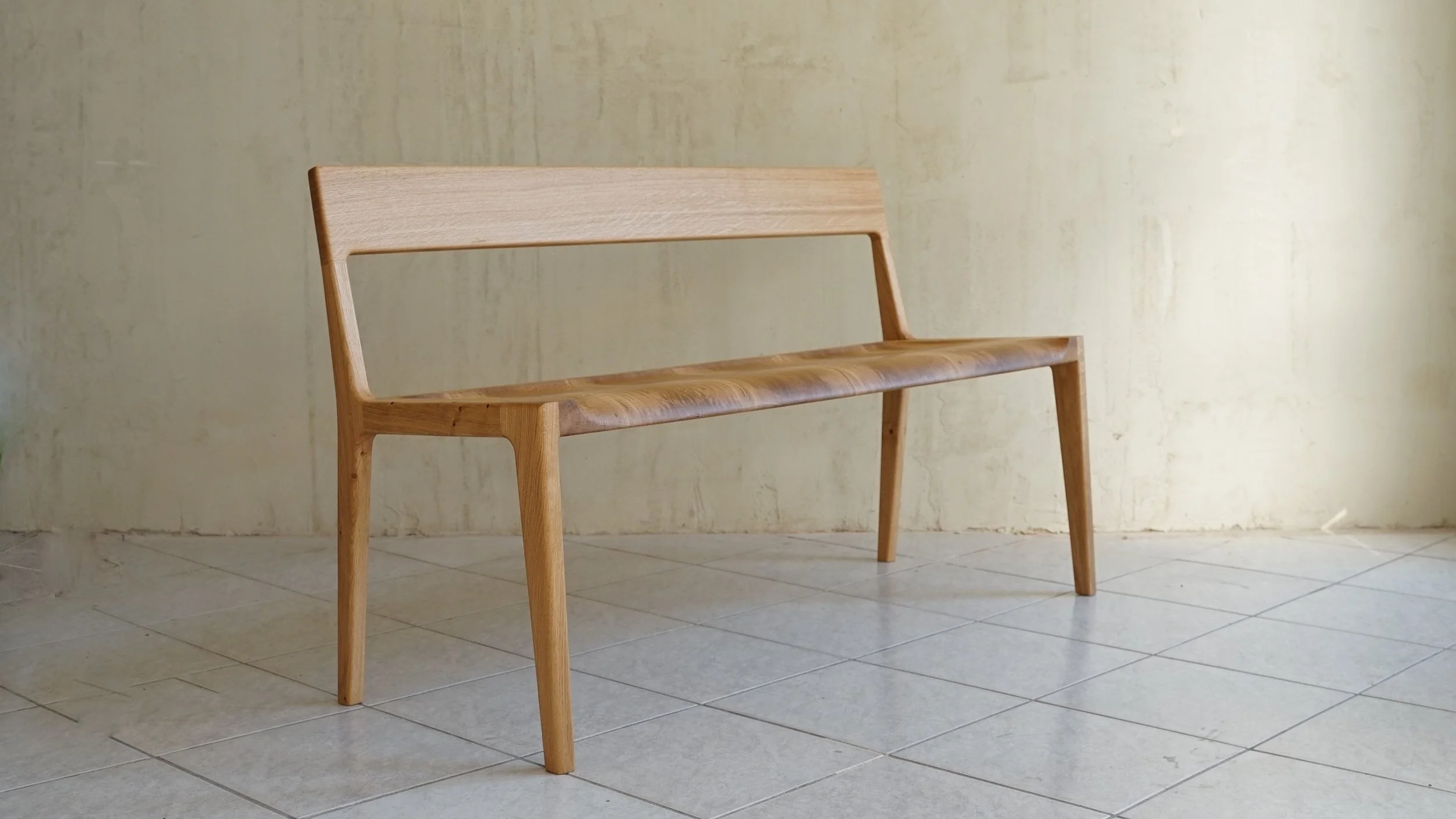 Ein hobelnder Holzbank mit gerader Rückenlehne in einem Raum mit gelblicher Wand und Fliesenboden.