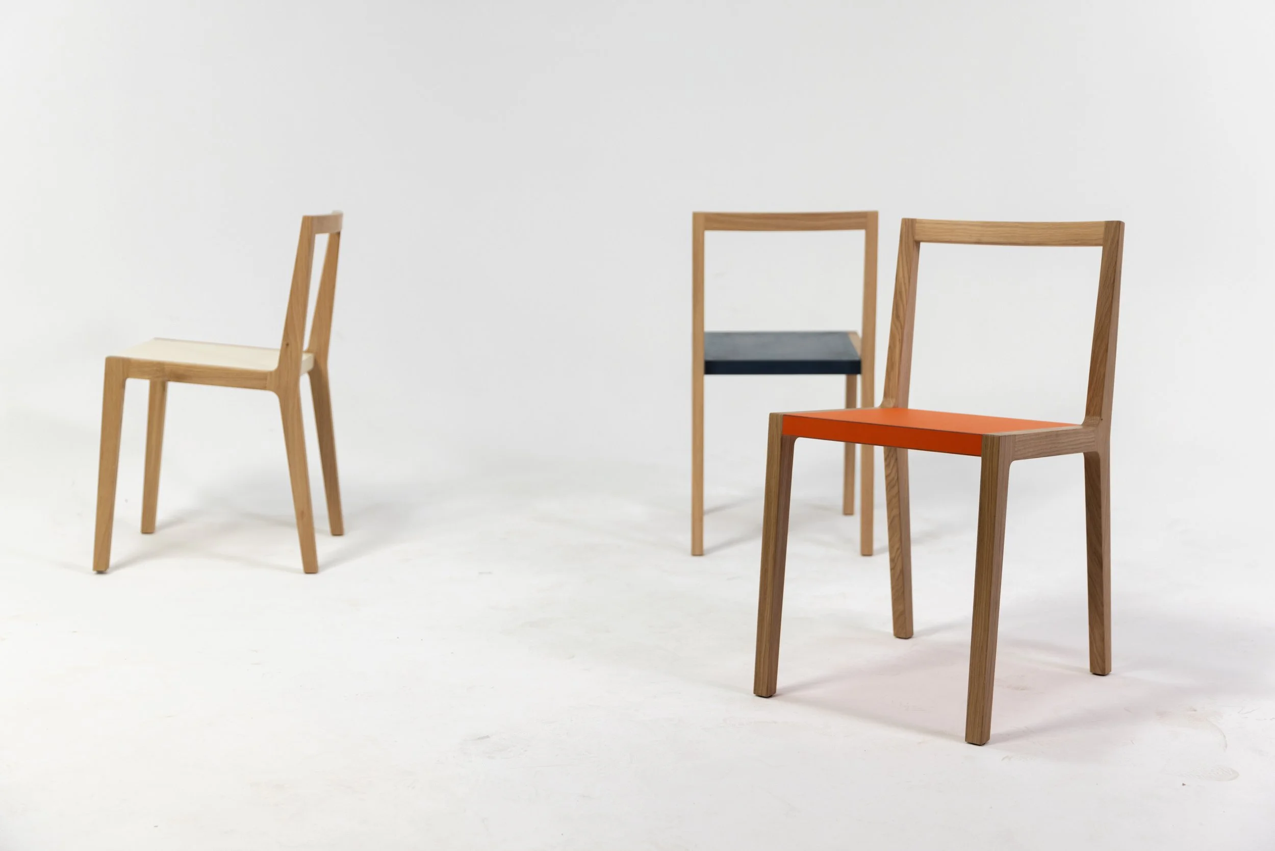 Vier moderne Stühle aus Holz mit bunten Sitzflächen, in einem weißen Raum