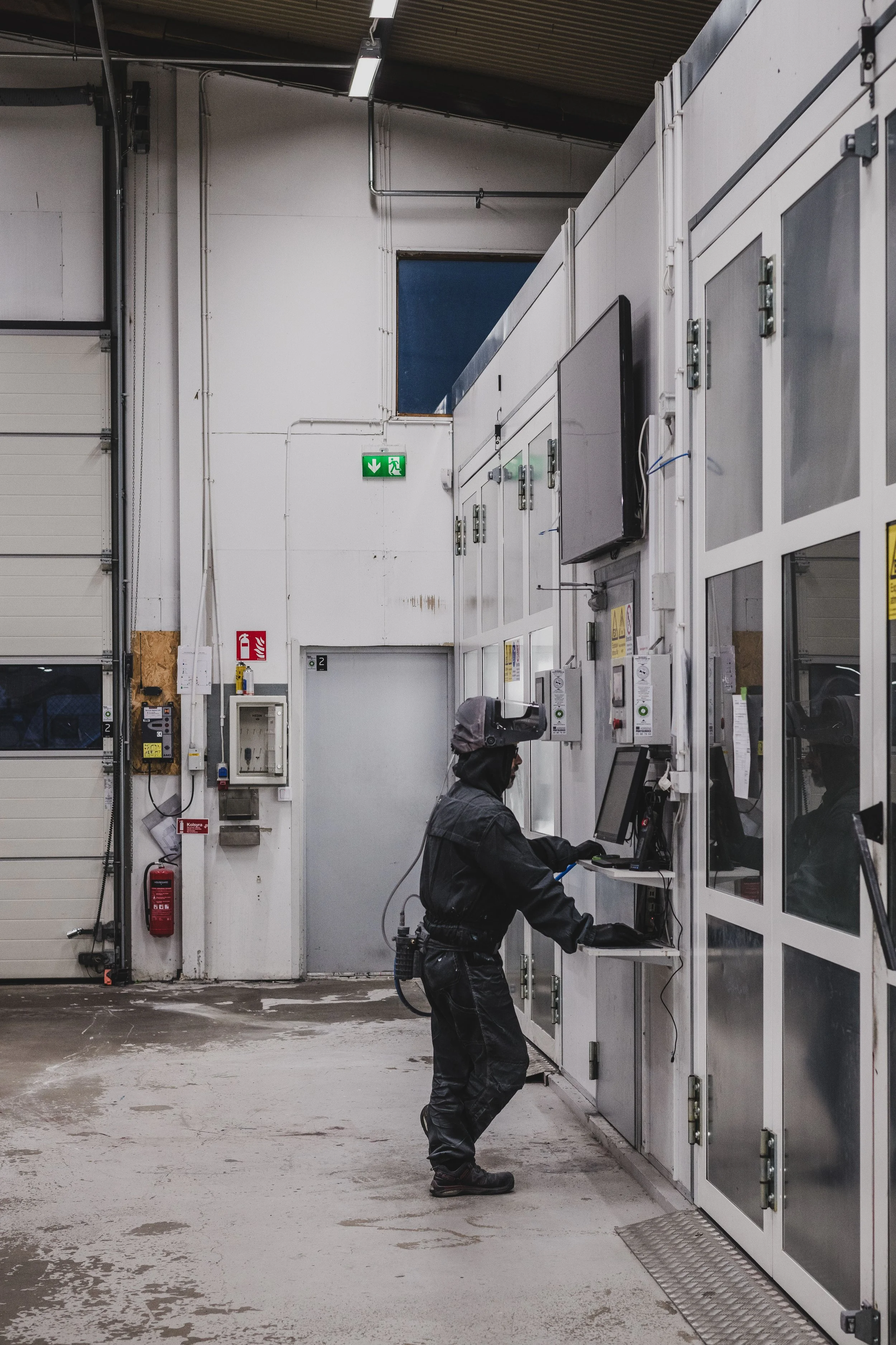 En person står framför en maskin i ett industriellt utrymme, vakar över en dator