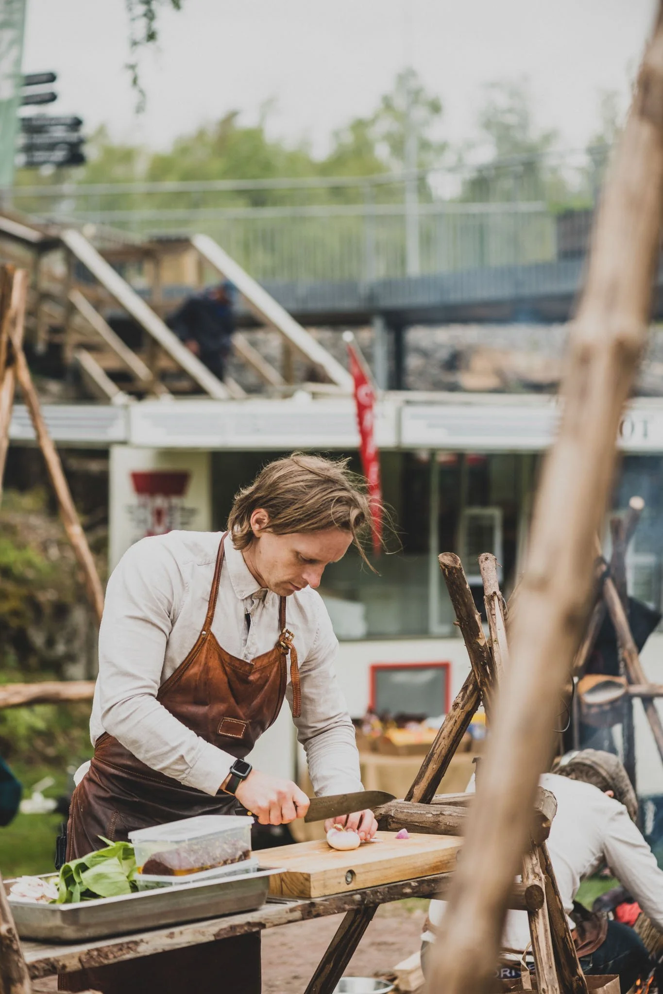 En person skär lök på en träbänk utomhus, med byggnadsställningar och personer i bakgrunden.