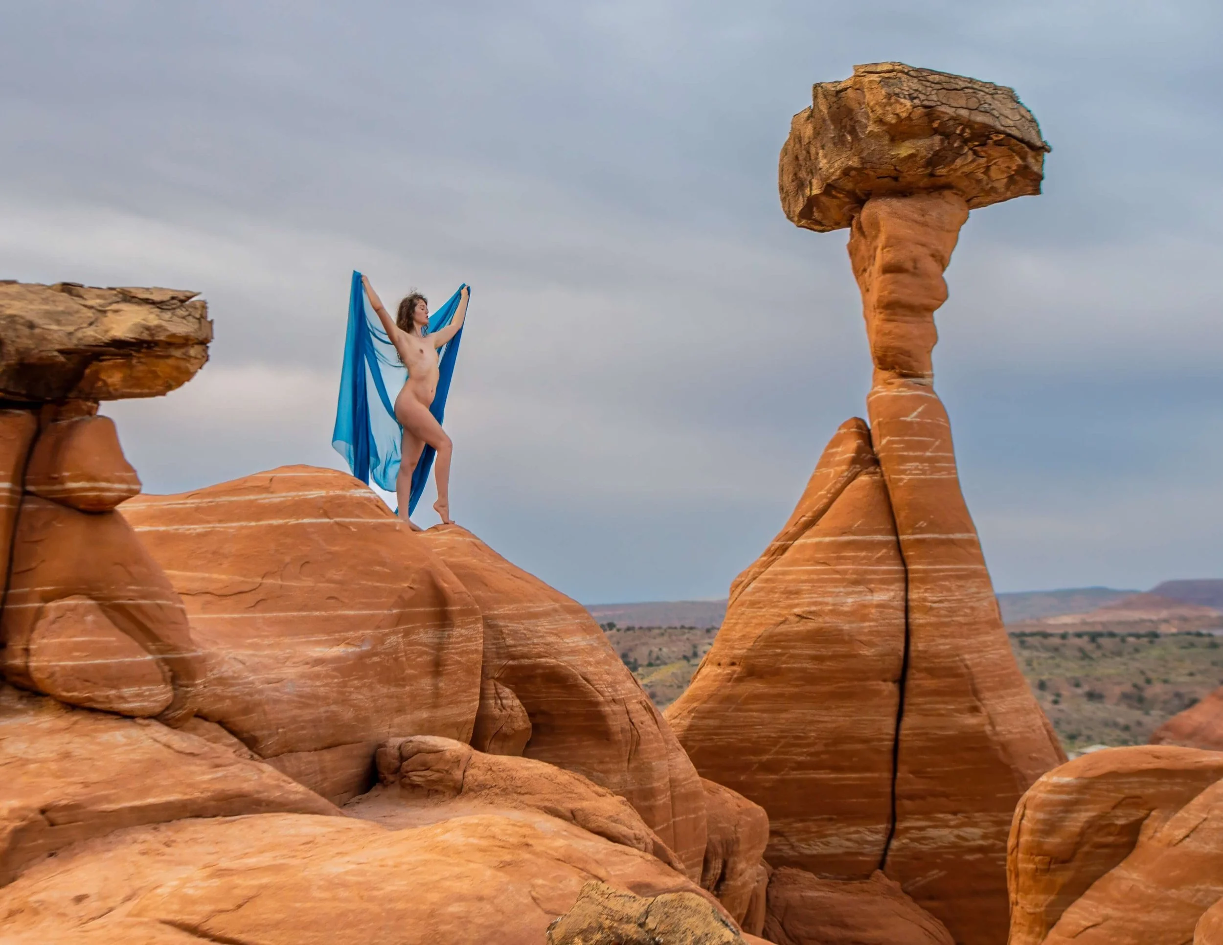 "Echoes on the Sandstone"
A lone lady climbs where eagles dare,
Arms outstretched to desert air.
In blue, a fleeting spark,
Framed by cliffs bold and stark.
Rocks, stark and ancient sentinels,
Hold secrets time no longer tells.
Curve - crevice, wind-