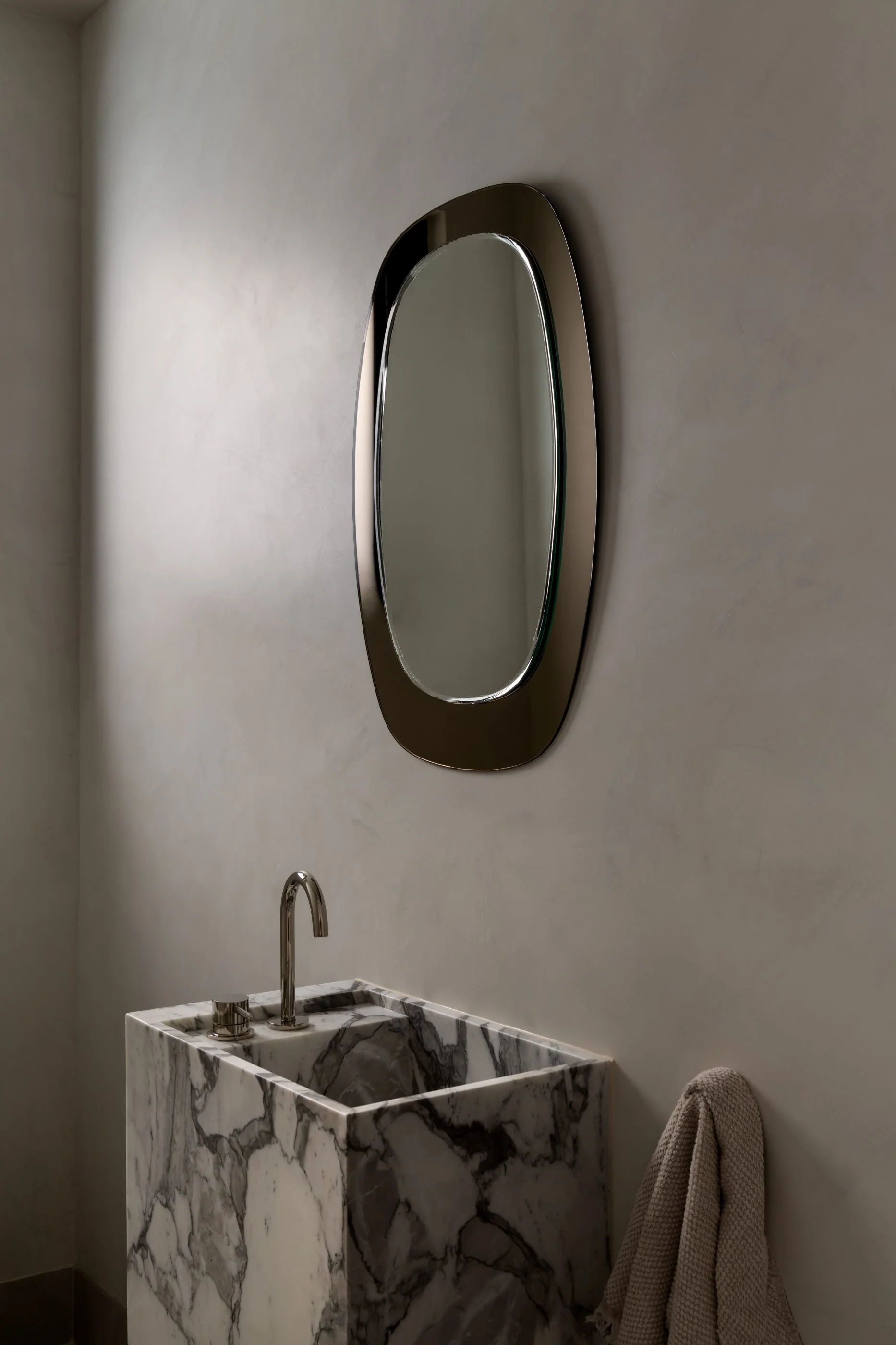 A modern bathroom with a marble sink, a wall-mounted mirror, a silver faucet, and a towel hanging on the wall.