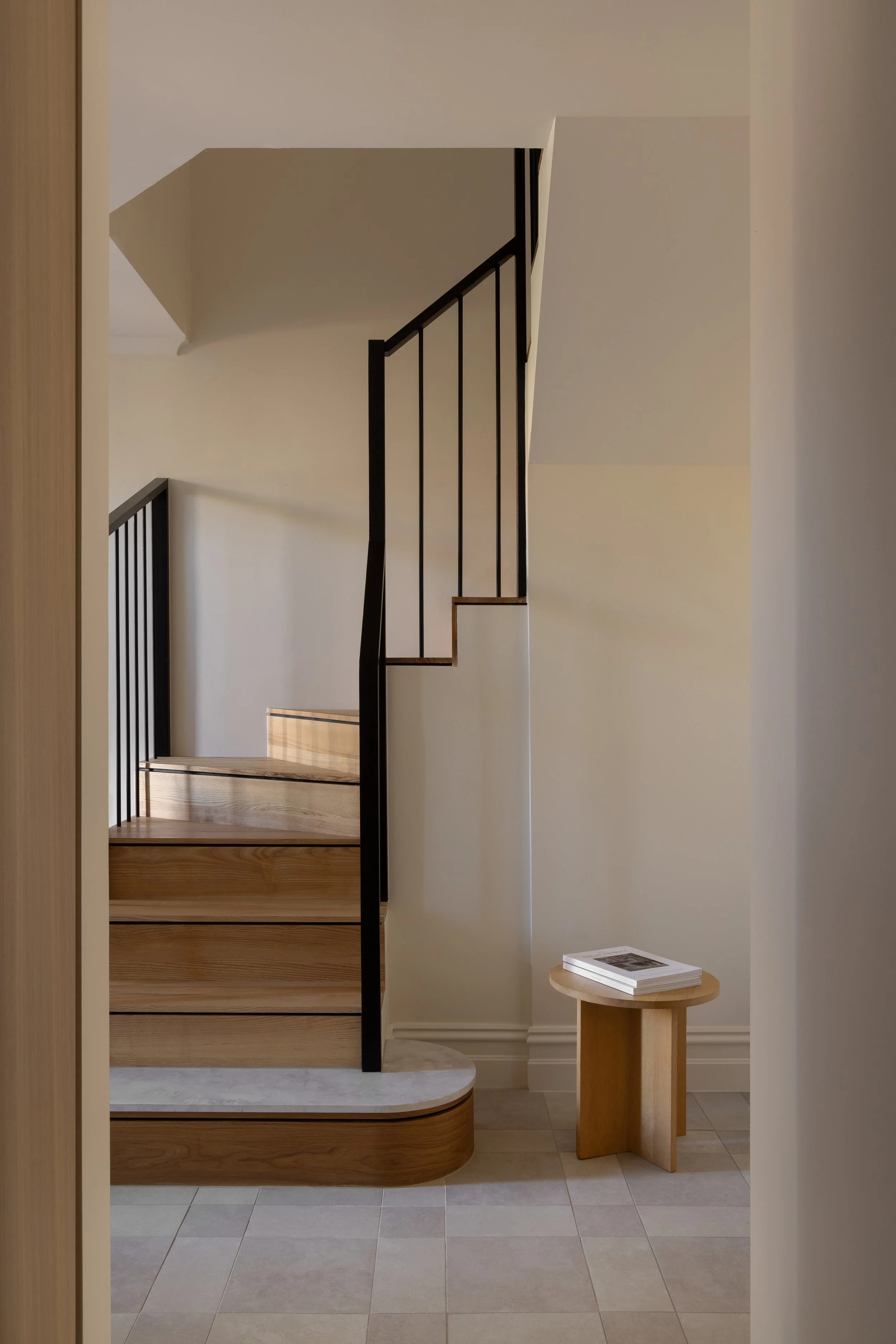 Minimalist staircase with wooden steps, black metal railing, and a small wooden side table with a book on it, in a modern home interior.