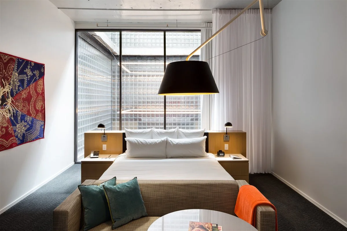 21c Oklahoma City guest room with decorative pendant lighting, integrated bedside lighting and large industrial window.