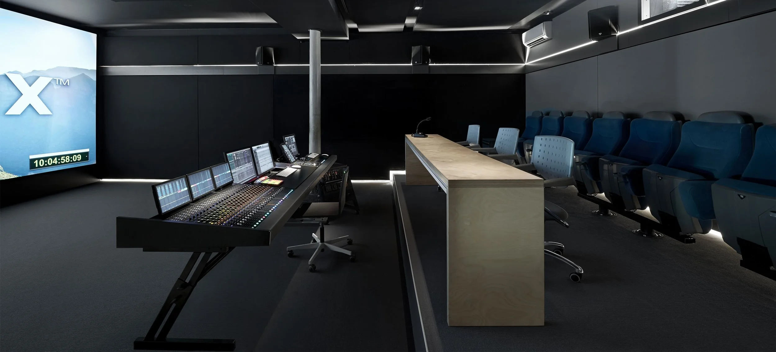 Empty modern conference or control room with a large screen display, audio mixing console, and seating area.