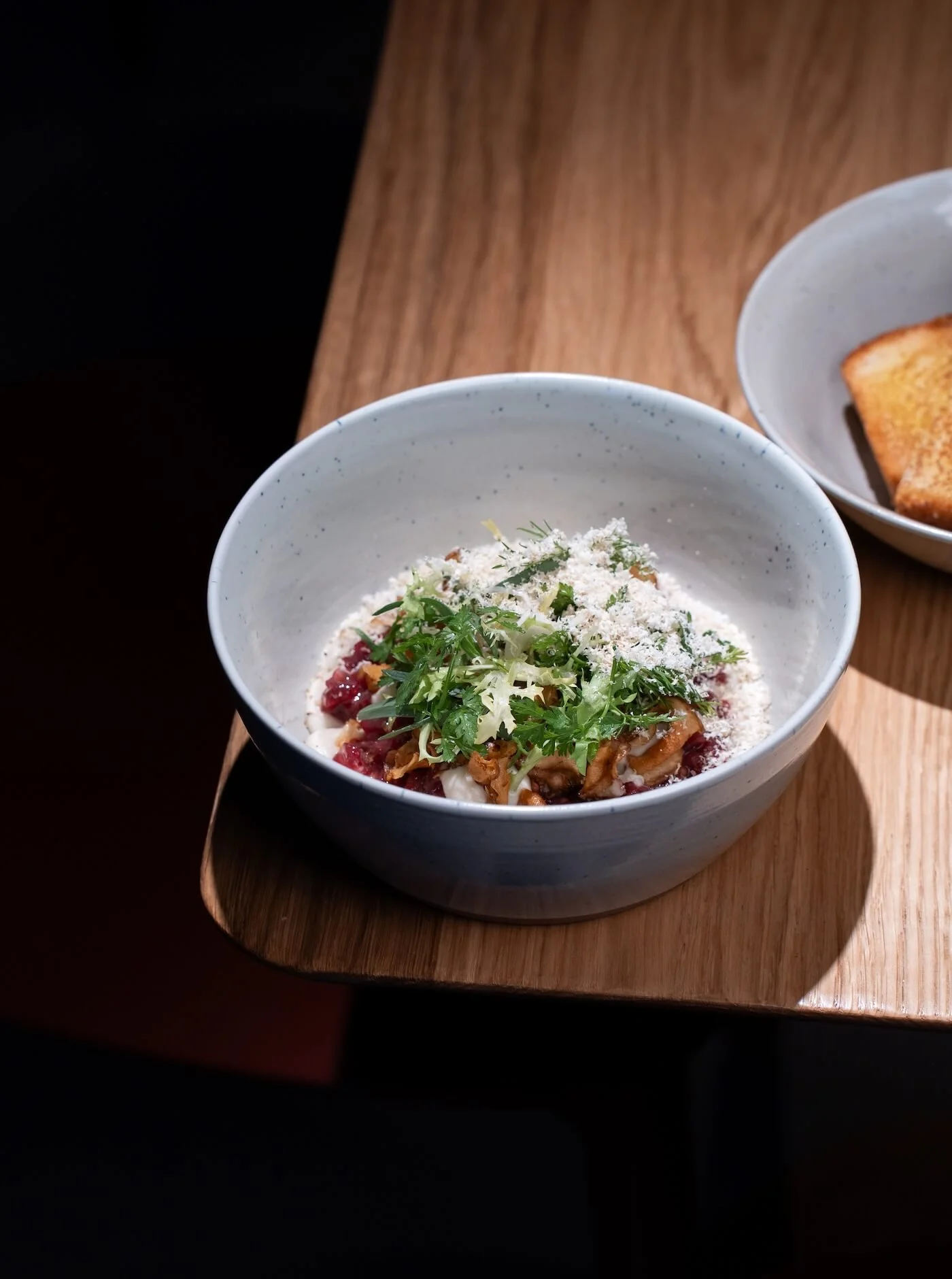 Neri’s new beef tartare, topped with mushrooms, fresh herbs, and finely grated garnish, served in a ceramic bowl with golden toast on the side.