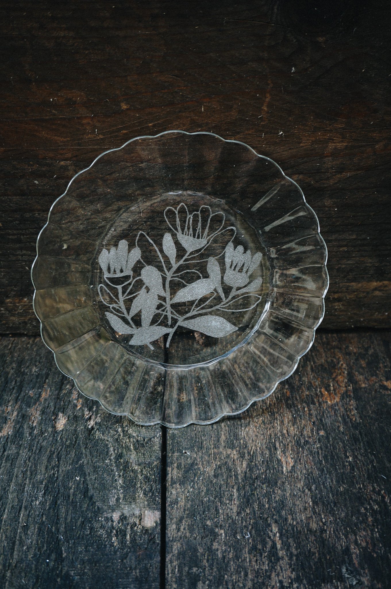 Assiette en verre avec motif floral gravé sur une table en bois sombre.