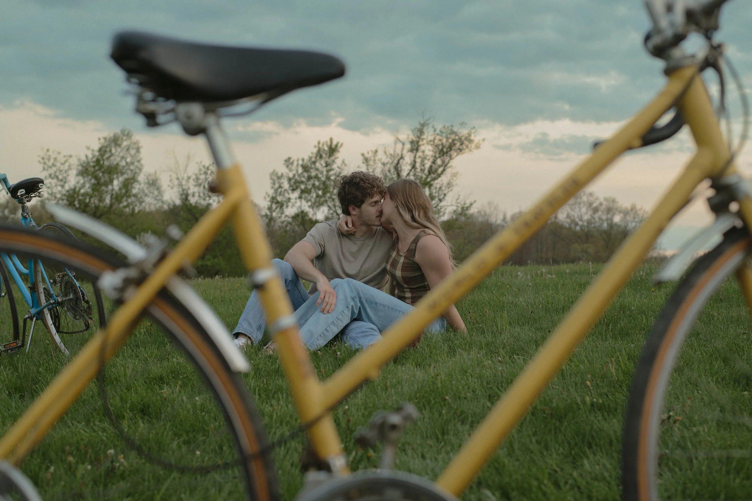 Couple smooching in a field with a bike in the foreground