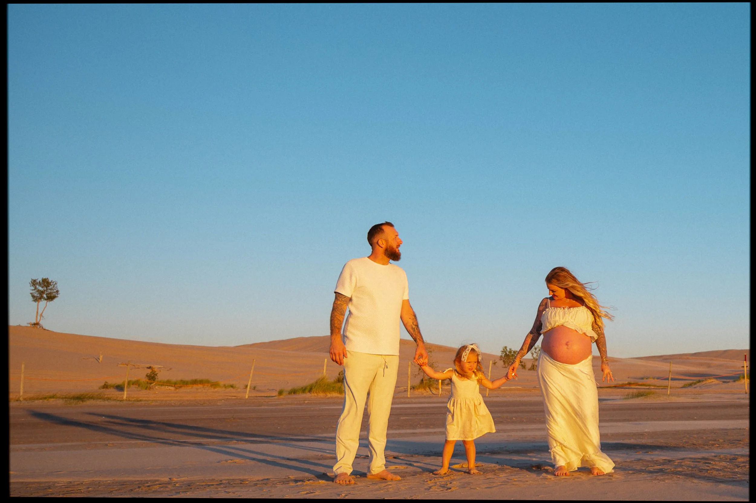 Maternity image of mom, dad, and a future big sister at the silver lake sand dunes during golden hour