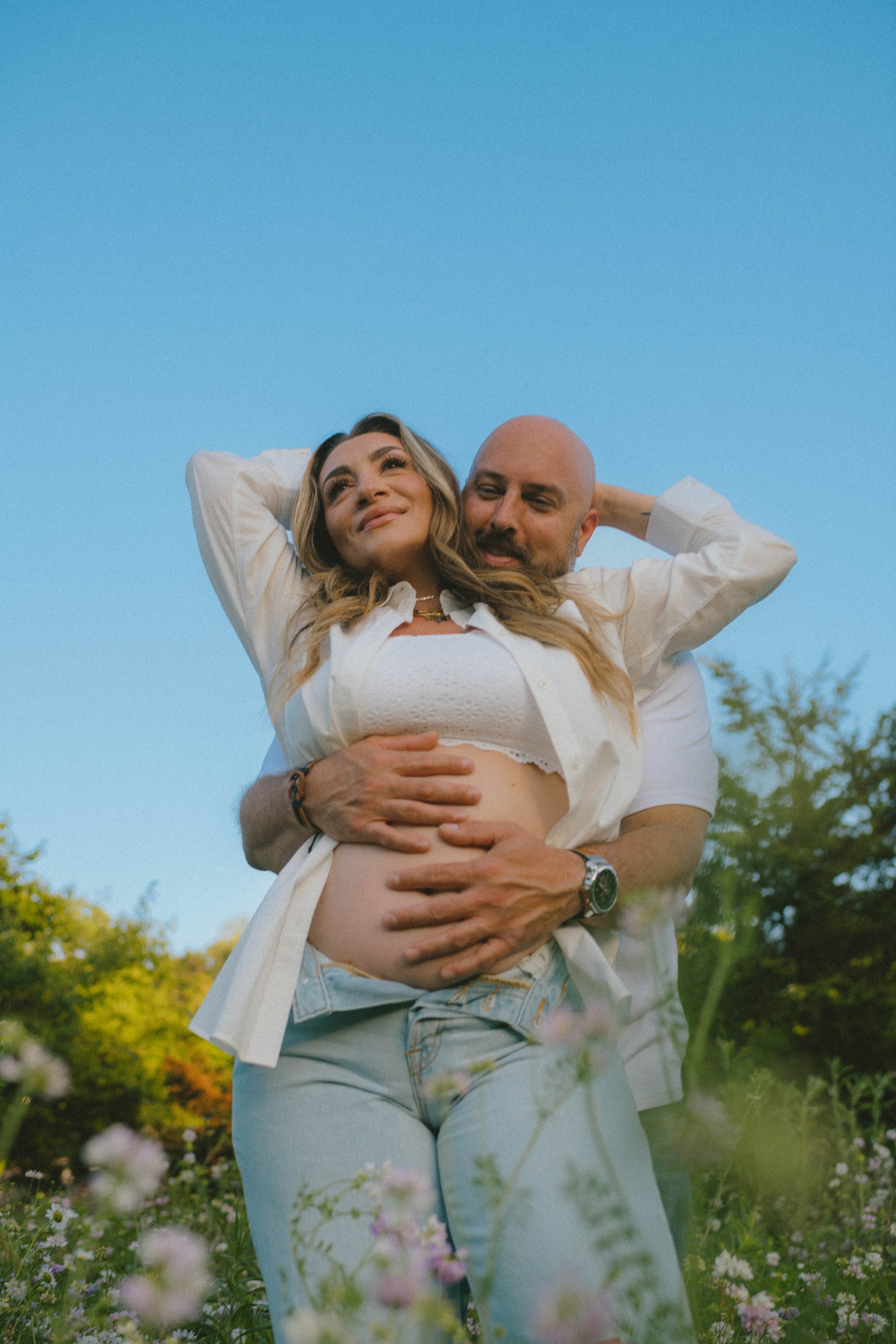 A dad to be snuggling up with momma to be in a flower field