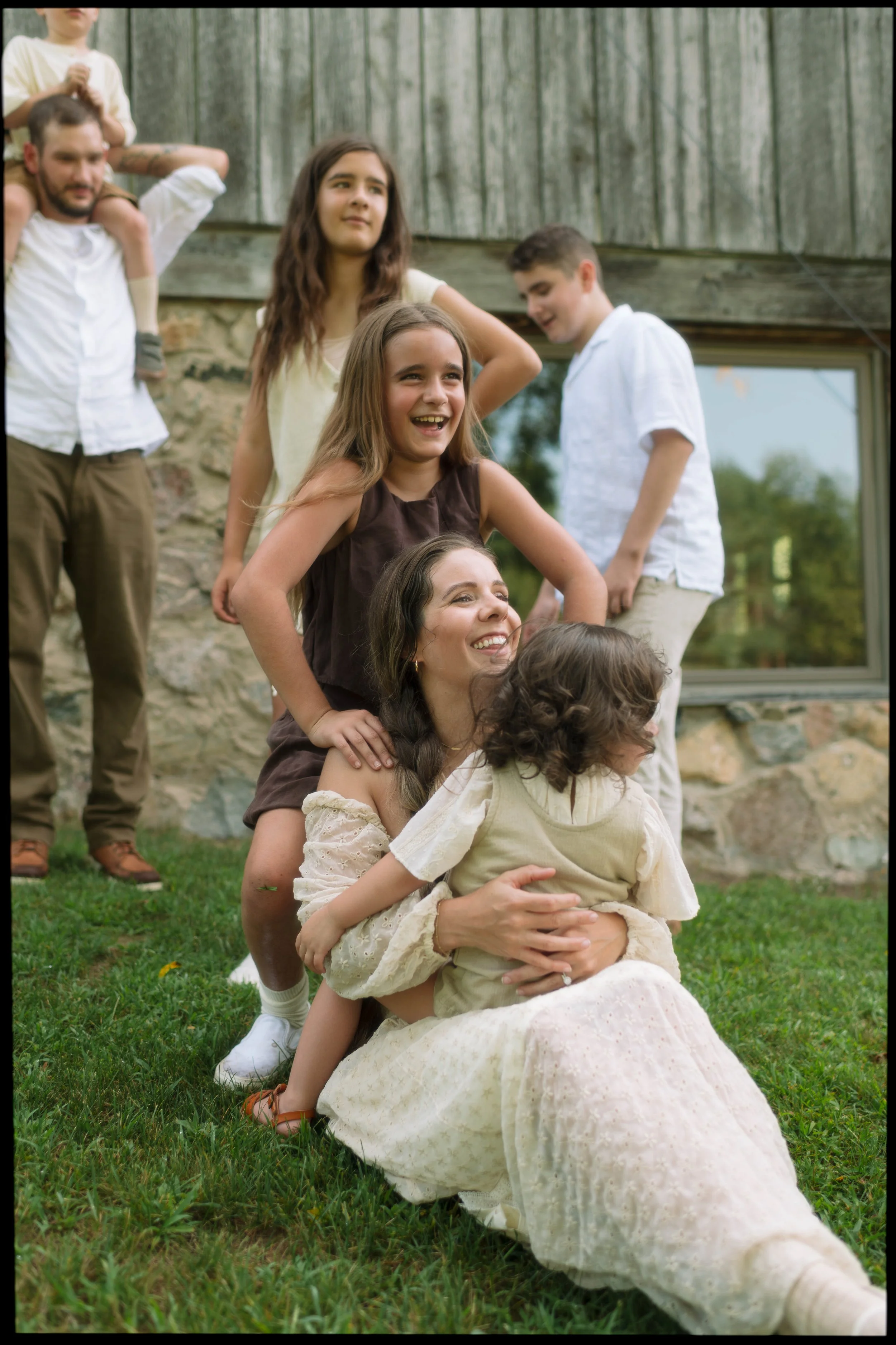 Family of 5 laughing and playing, child on dads shoulders, sitting in moms lap and lining up behind and beside them.