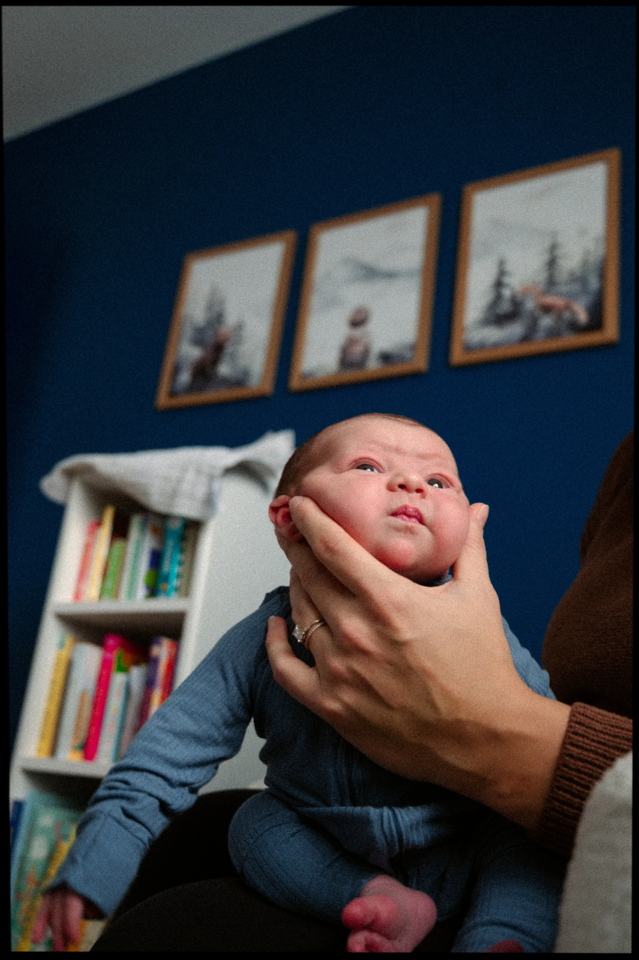 Photo of newborn, lifestyle image, baby chunky cheeks in a blue room held by mom, image is shot from below