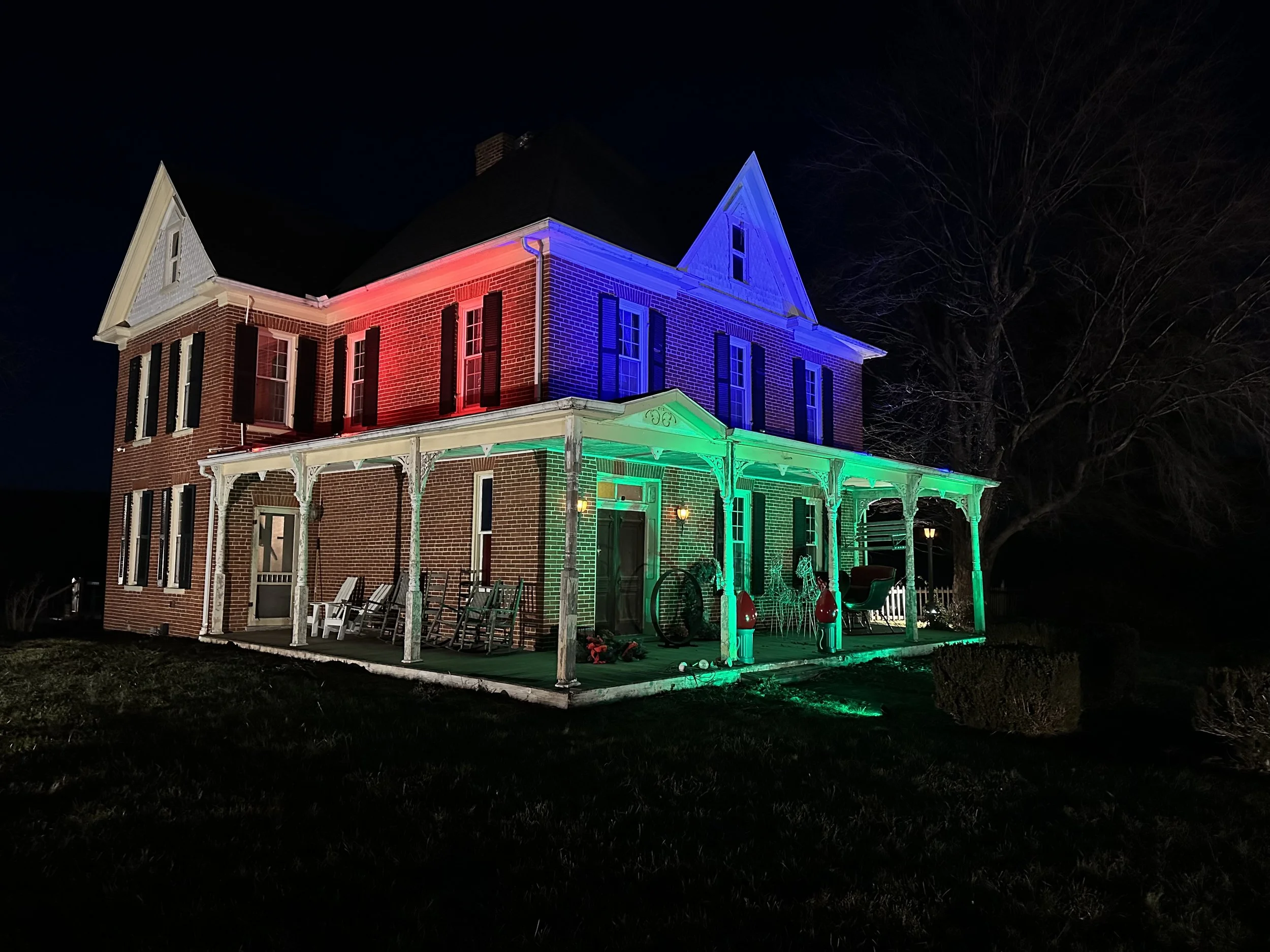 Red, Blue, Green, and White landscaping lights on a brick house 