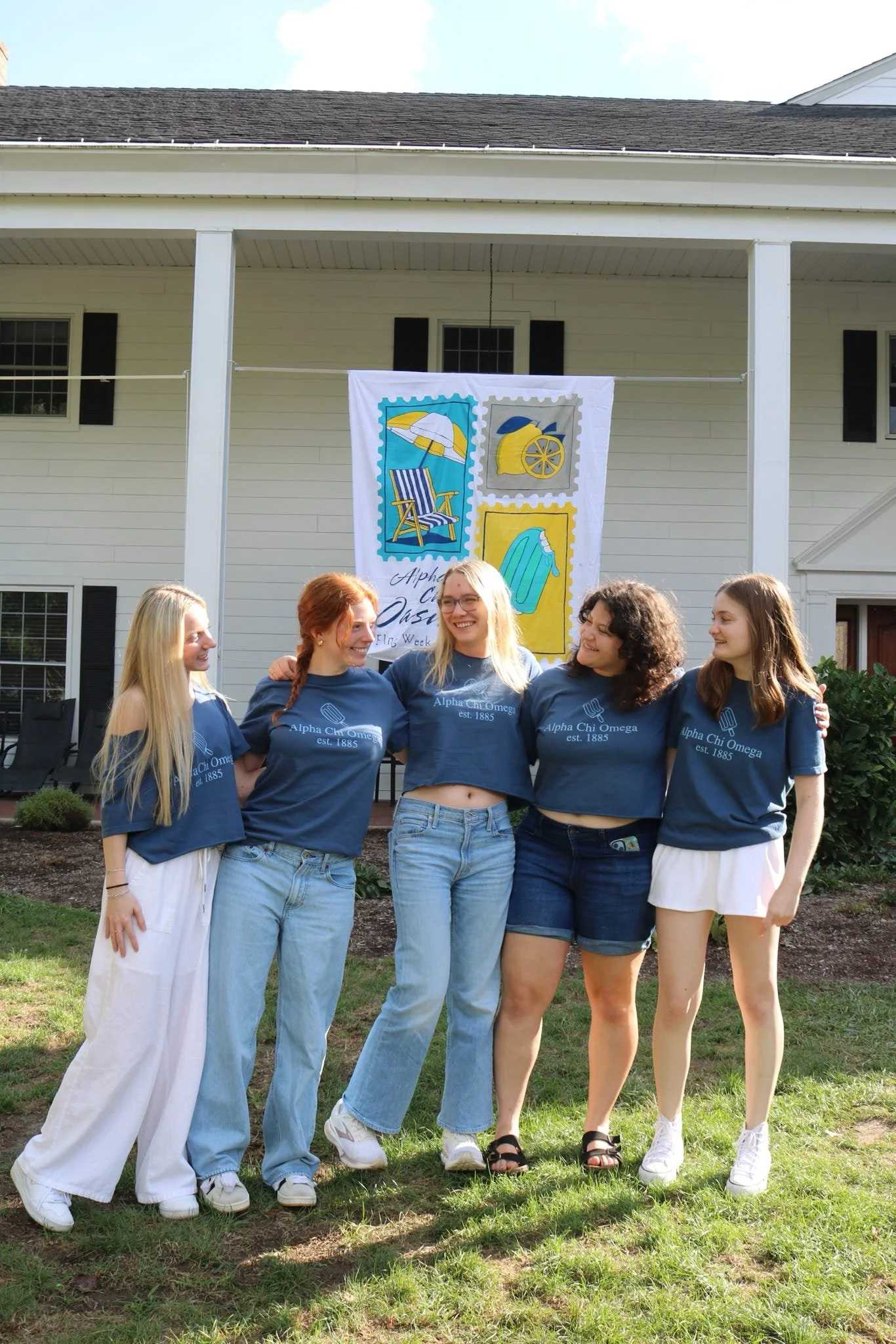 Four young women standing outdoors, smiling, at a graduation celebration, with a modern building and trees in the background.