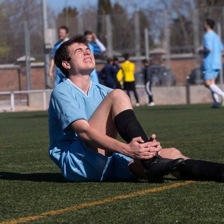 Football player holding his ankle after injury, suitable for sports injury recovery physiotherapy at Kerala Ayurveda Clinic Leicester for strains, sprains and tendon issues.