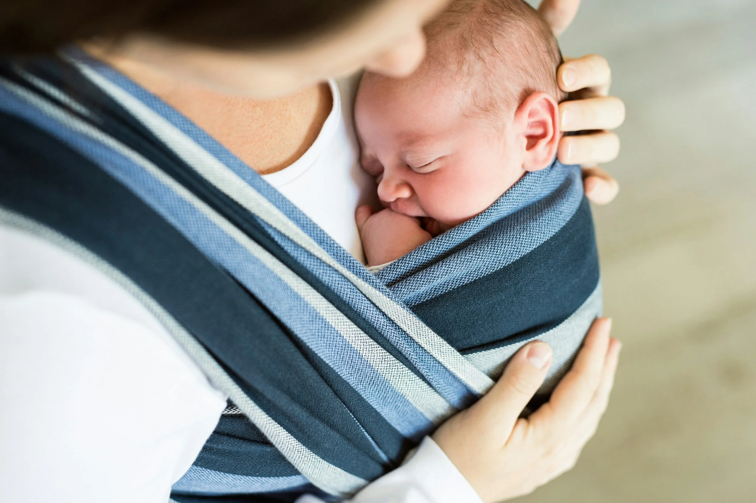 Baby sleeping in their mother's blue baby carrier.