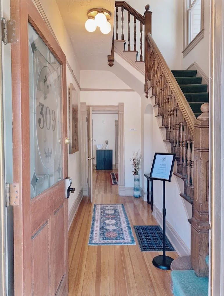 Entrance and hallway at Walls Counseling in Colorado Springs, featuring a wooden front door, runner rug, staircase, and welcoming interior leading to therapy rooms.