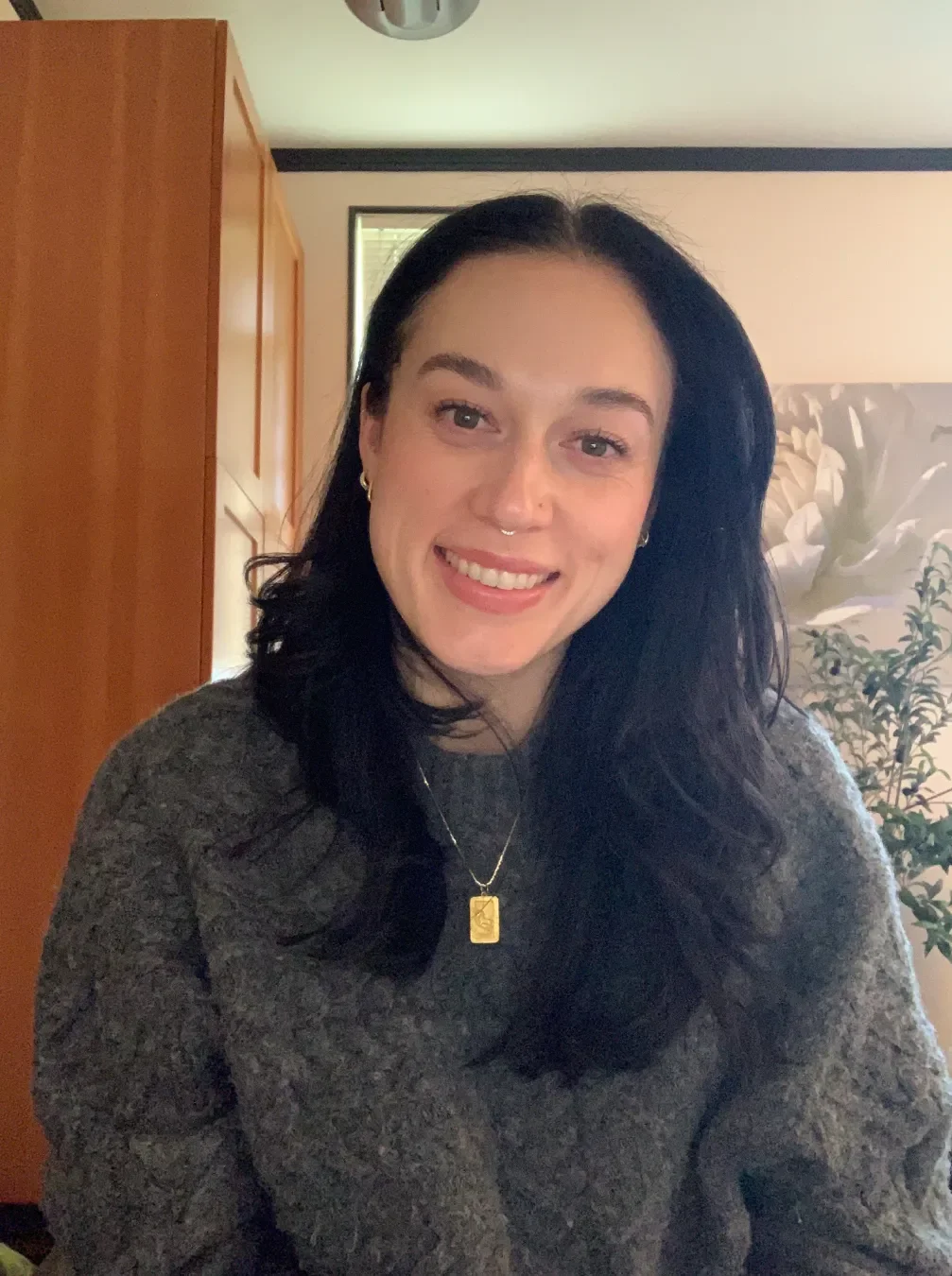 Kim Pia is a female presenting person with dark hair. She's wearing a gray sweater and a gold necklace.