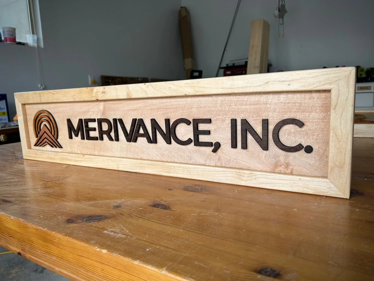 Wooden sign with the logo and name of MERVANCE, INC. engraved in black.
