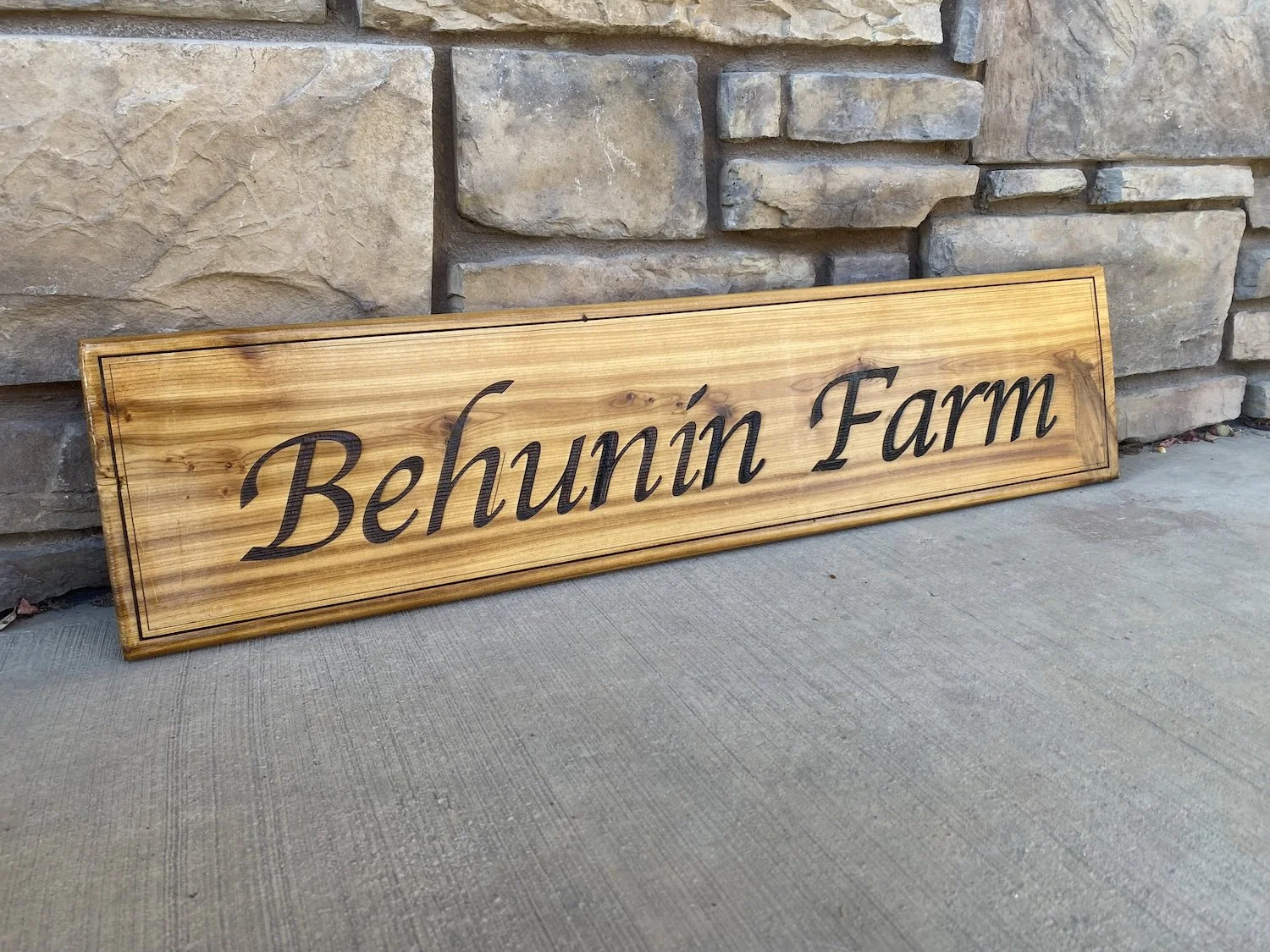 A wooden sign with the words 'Behunin Farm' engraved on it, leaning against a stone wall.