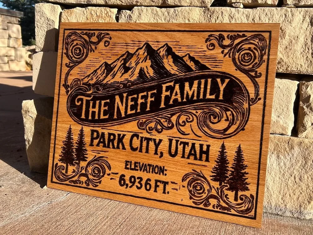 Wooden signboard with engraved mountains, trees, swirls, and the text "The Neff Family, Park City, Utah, Elevation: 6,936 ft" burnt in black.