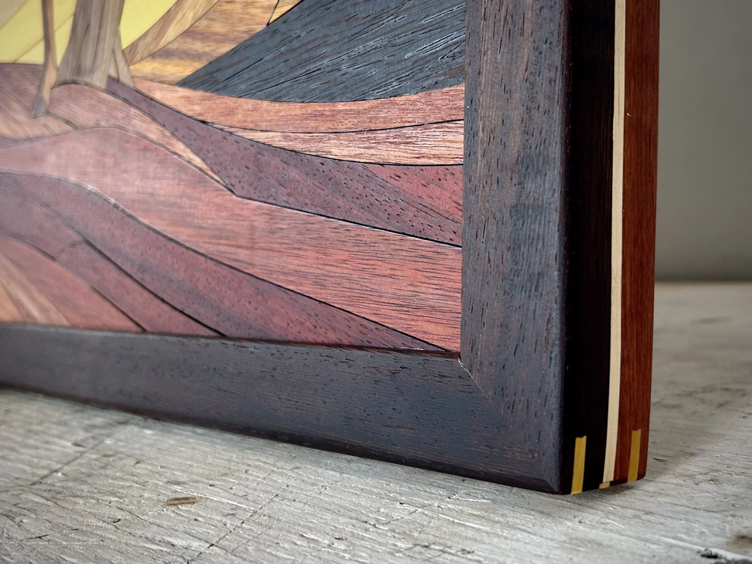 Close-up of a wooden furniture piece featuring different types of wood with distinct colors and grain patterns, placed on a gray wooden surface.