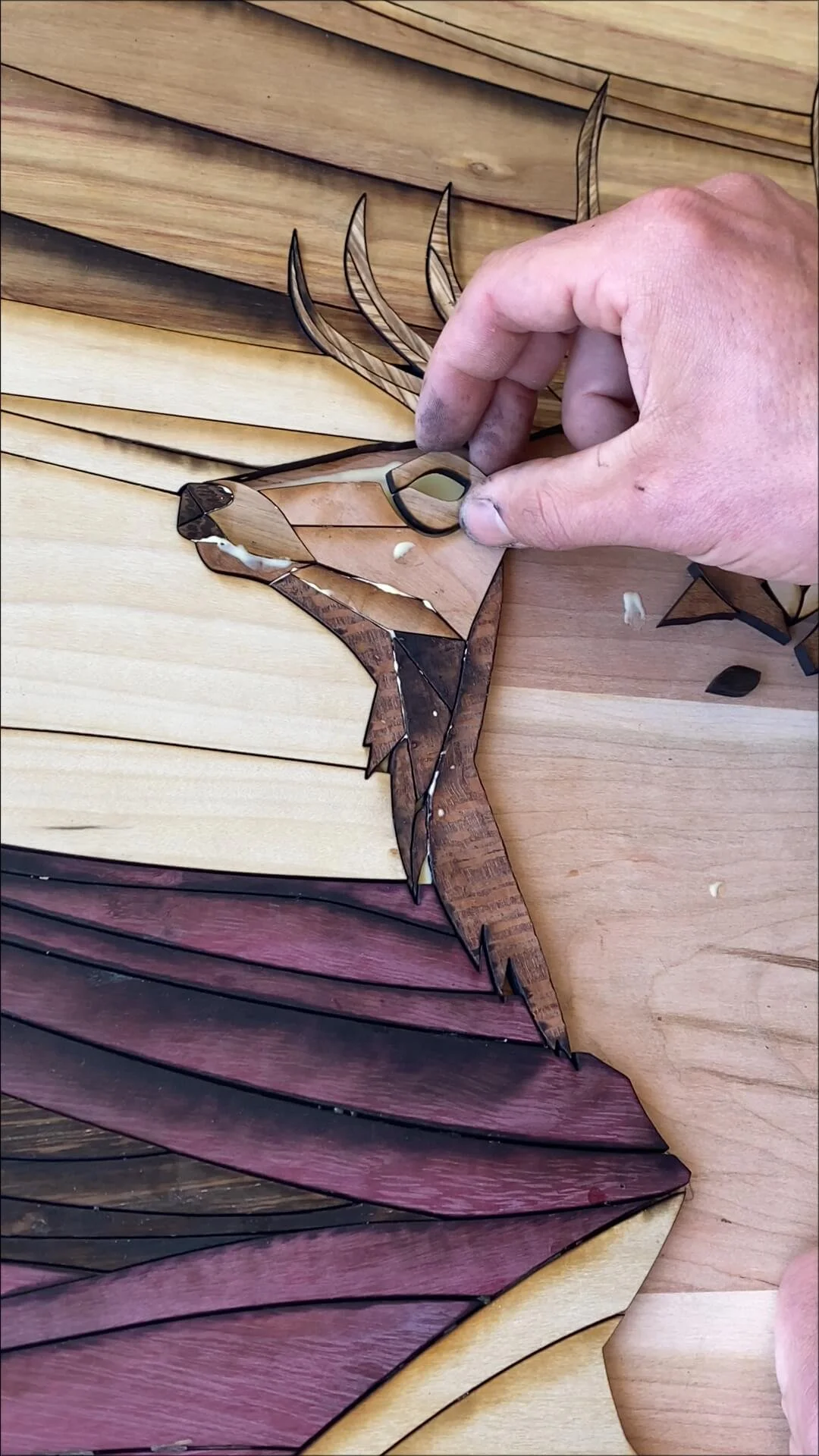 Image of a person assembling a wooden mosaic of a bird with colorful wooden pieces, including shades of brown, yellow, and purple, on a wooden surface.