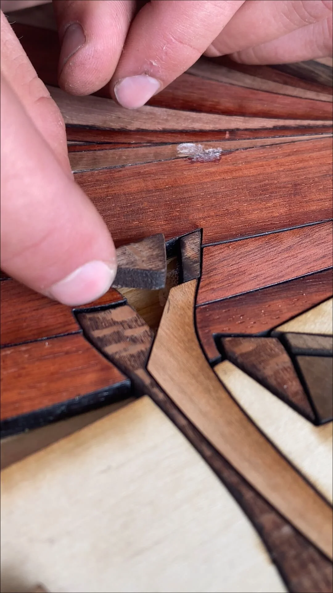 Close-up of a person's hand working on a wooden mosaic puzzle, placing or adjusting a piece.