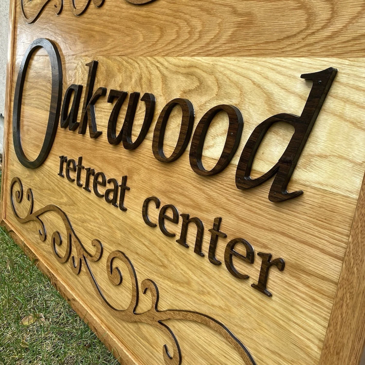 Wooden sign with the text 'Oakwood retreat center' in large black letters, and a decorative flourish below, displayed outdoors on grass.