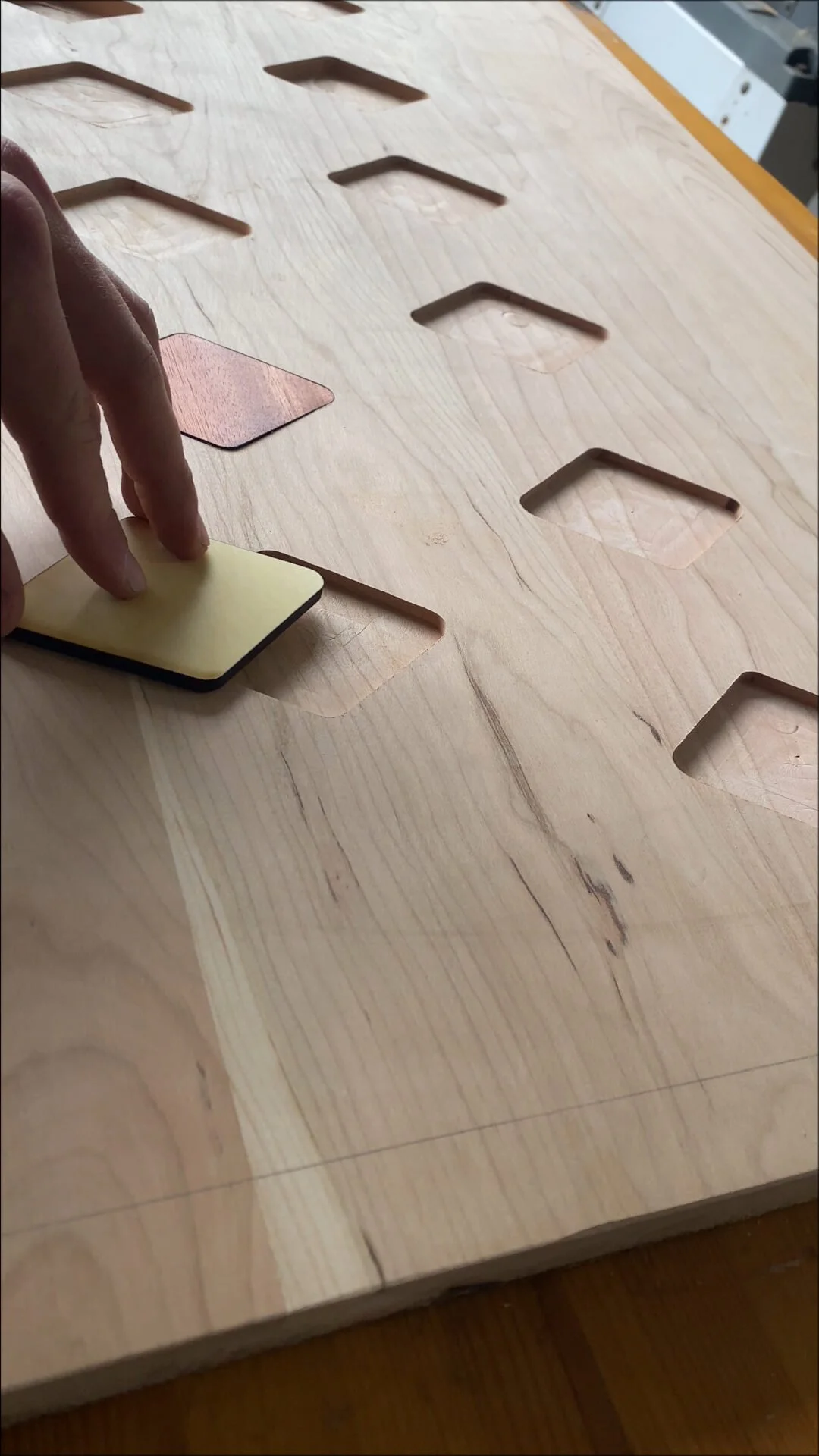 Person sanding a wooden surface with a sanding pad, working on multiple rectangular slots in the wood.