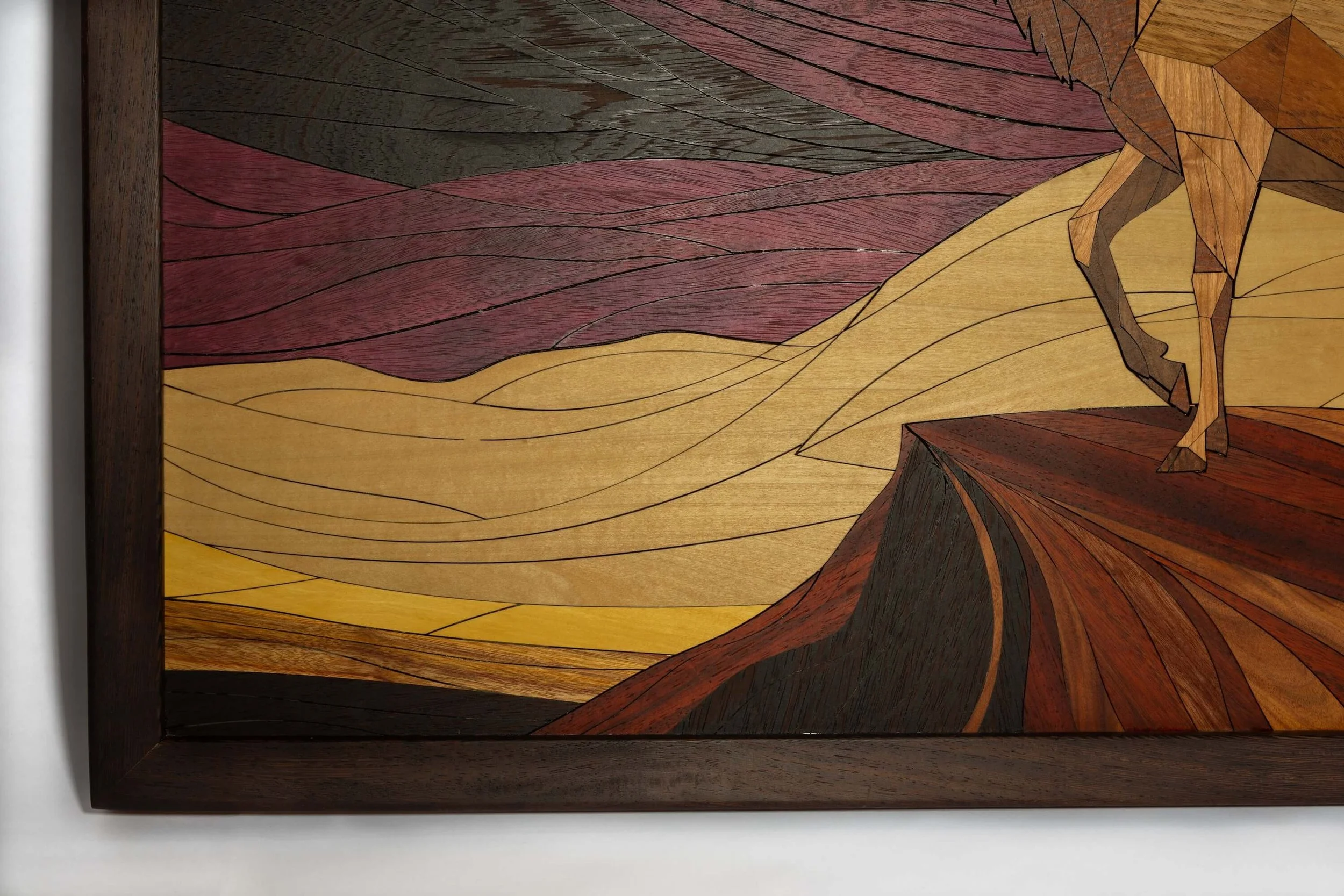Close-up of a wooden artwork with various colored wood pieces arranged to depict a mountain landscape scene.