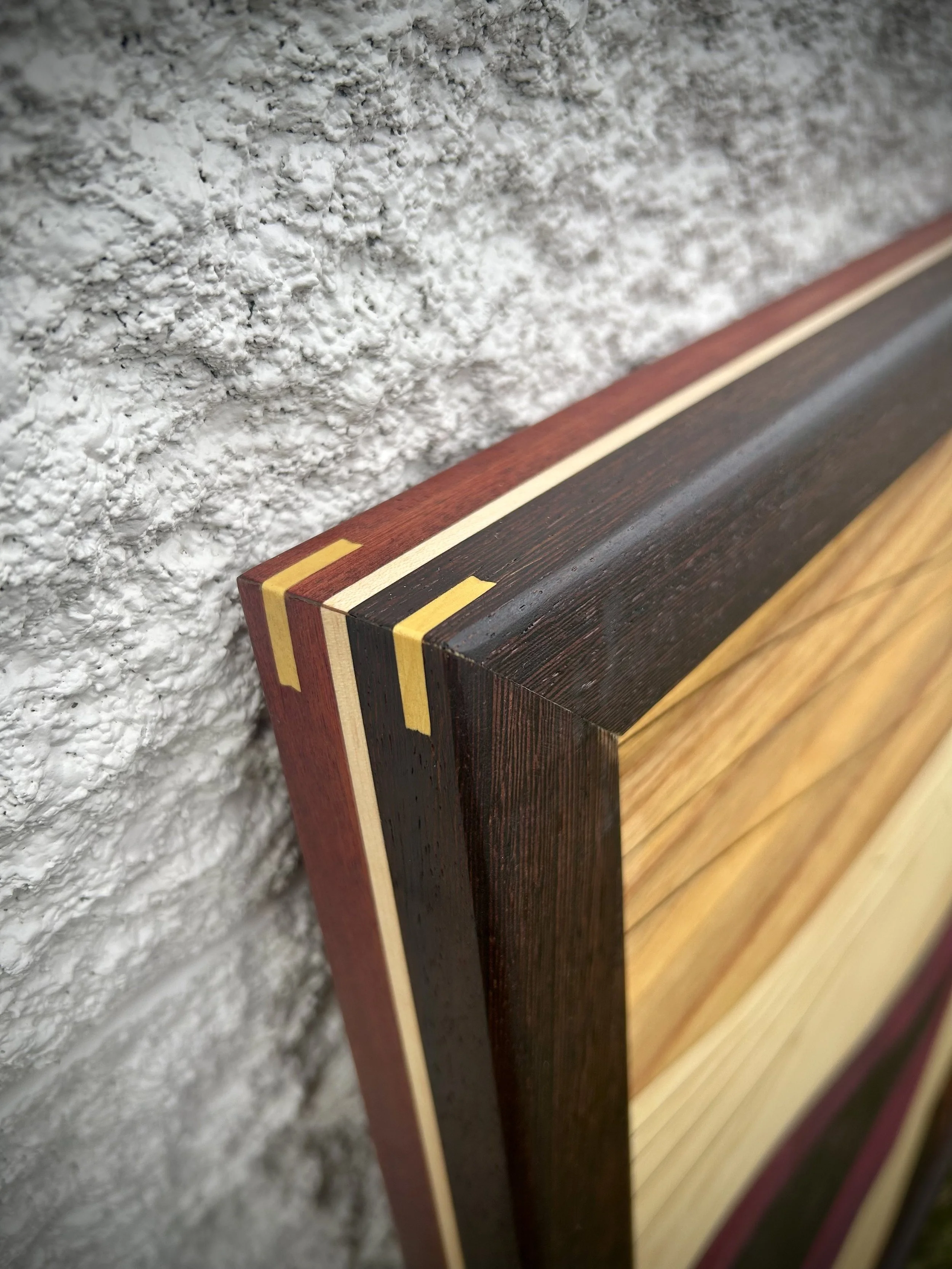 Close-up of a wooden frame with multiple colored layers mounted on a textured wall.