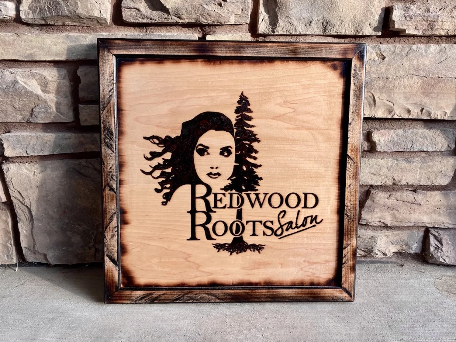 Wooden sign with a woman's face and pine trees, reading "Redwood Roots Salm".