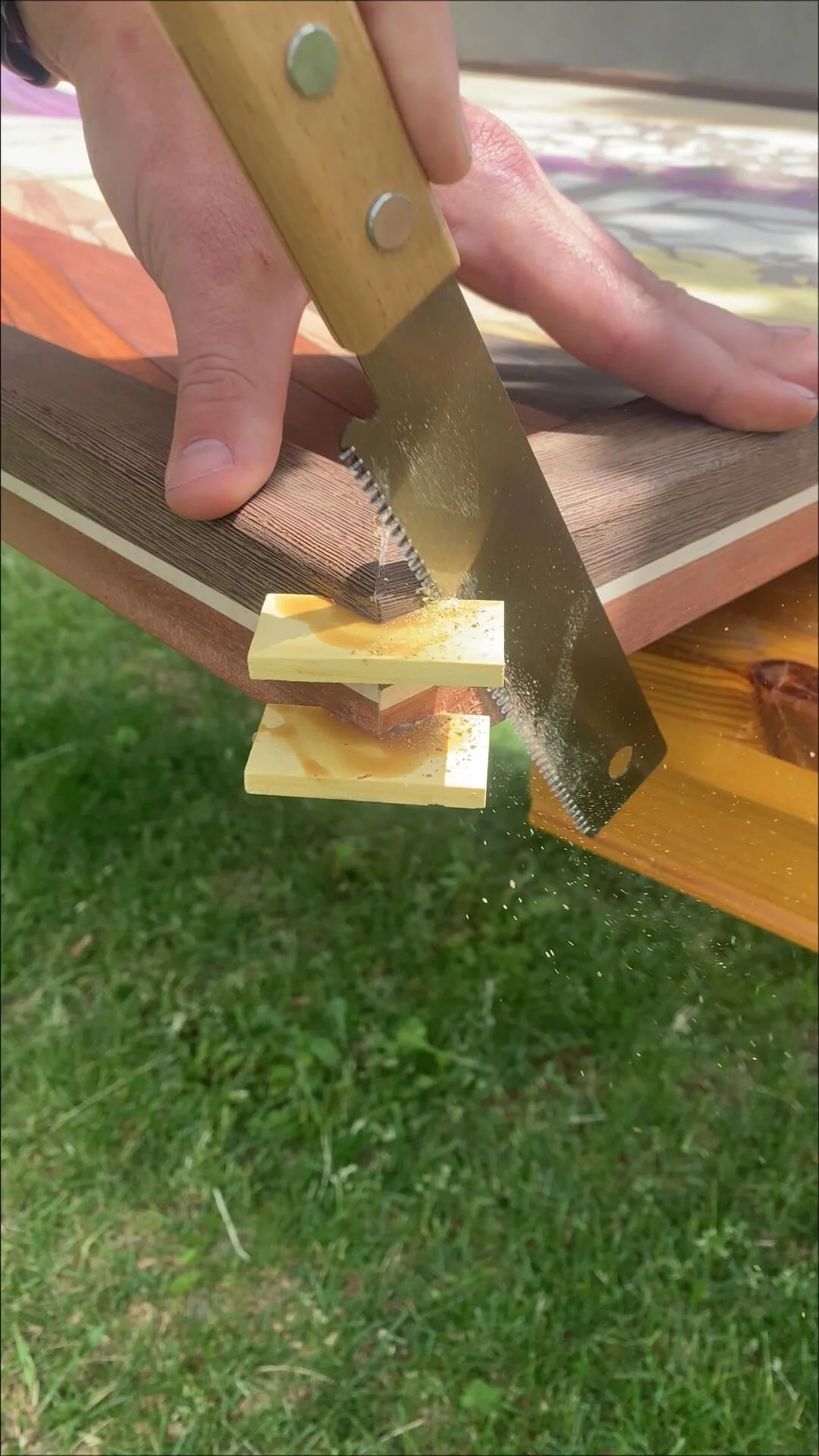 Person sawing wood outdoors with a hand saw, with wood shavings flying.