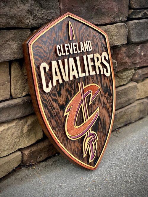 A Cleveland Cavaliers wooden shield sign leaning against a stone wall, featuring the team's logo and name.