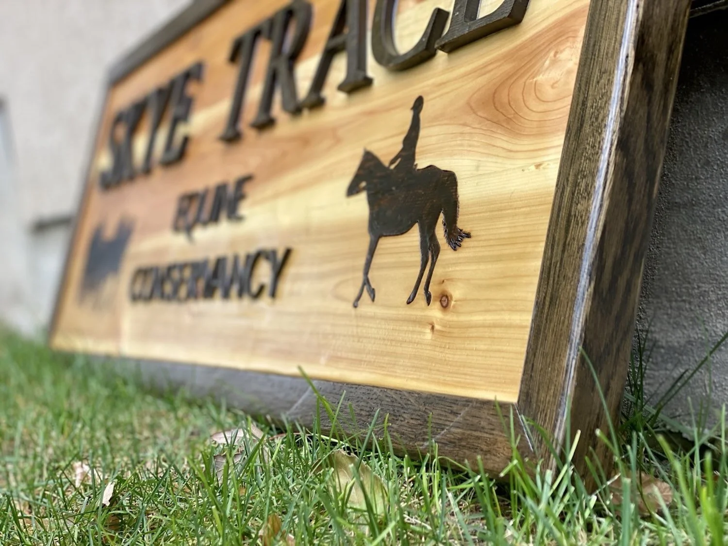 Wooden sign with black raised letters and a black silhouette of a horse.