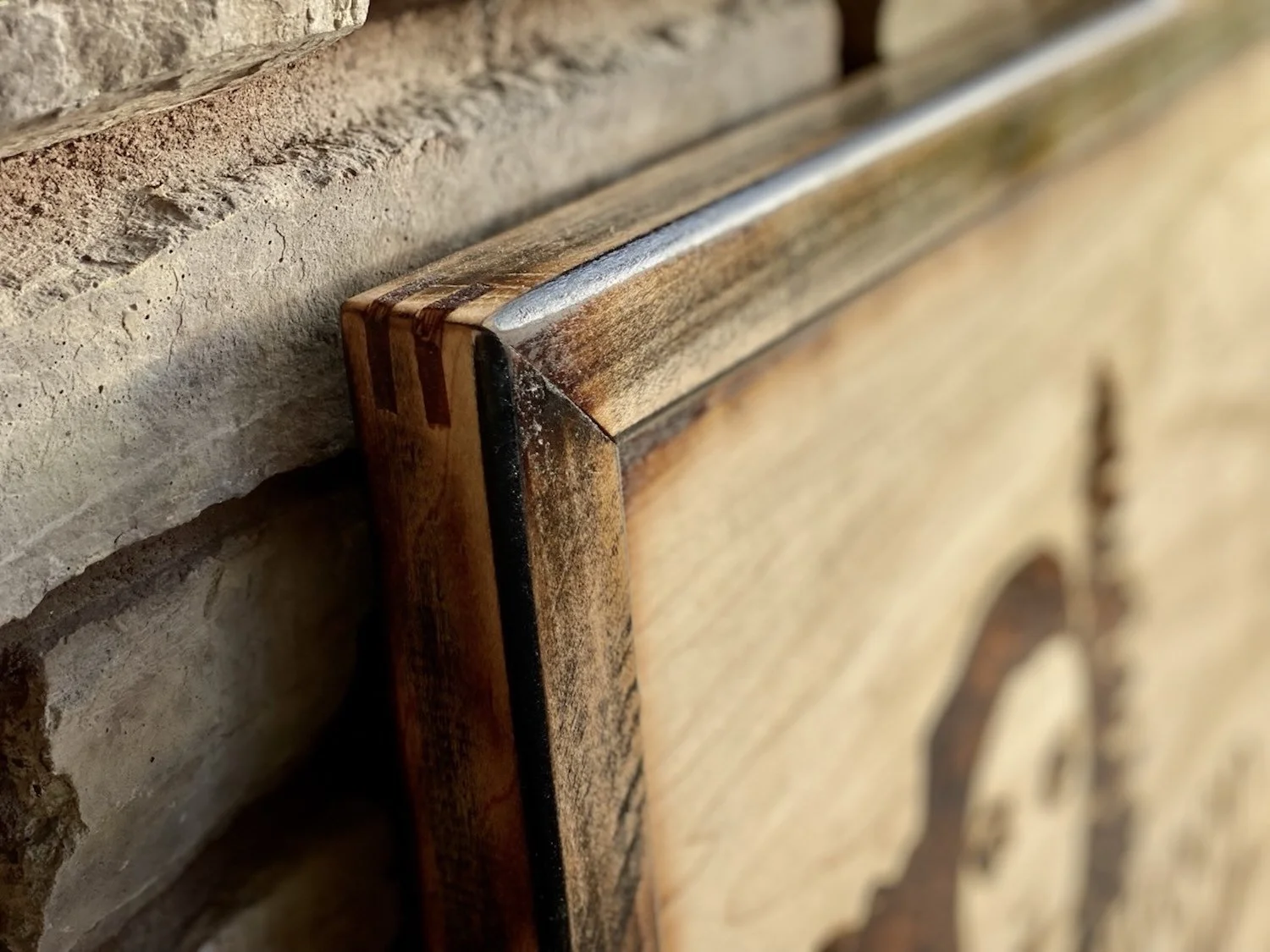 Close-up of a wooden sign frame with a spine joinery, mounted on a brick wall.