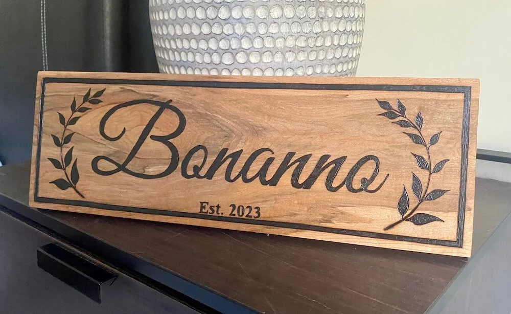 Wooden sign with the word "Bananno" written in cursive, decorated with leaf drawings on each side, and the text "Est. 2023" underneath.