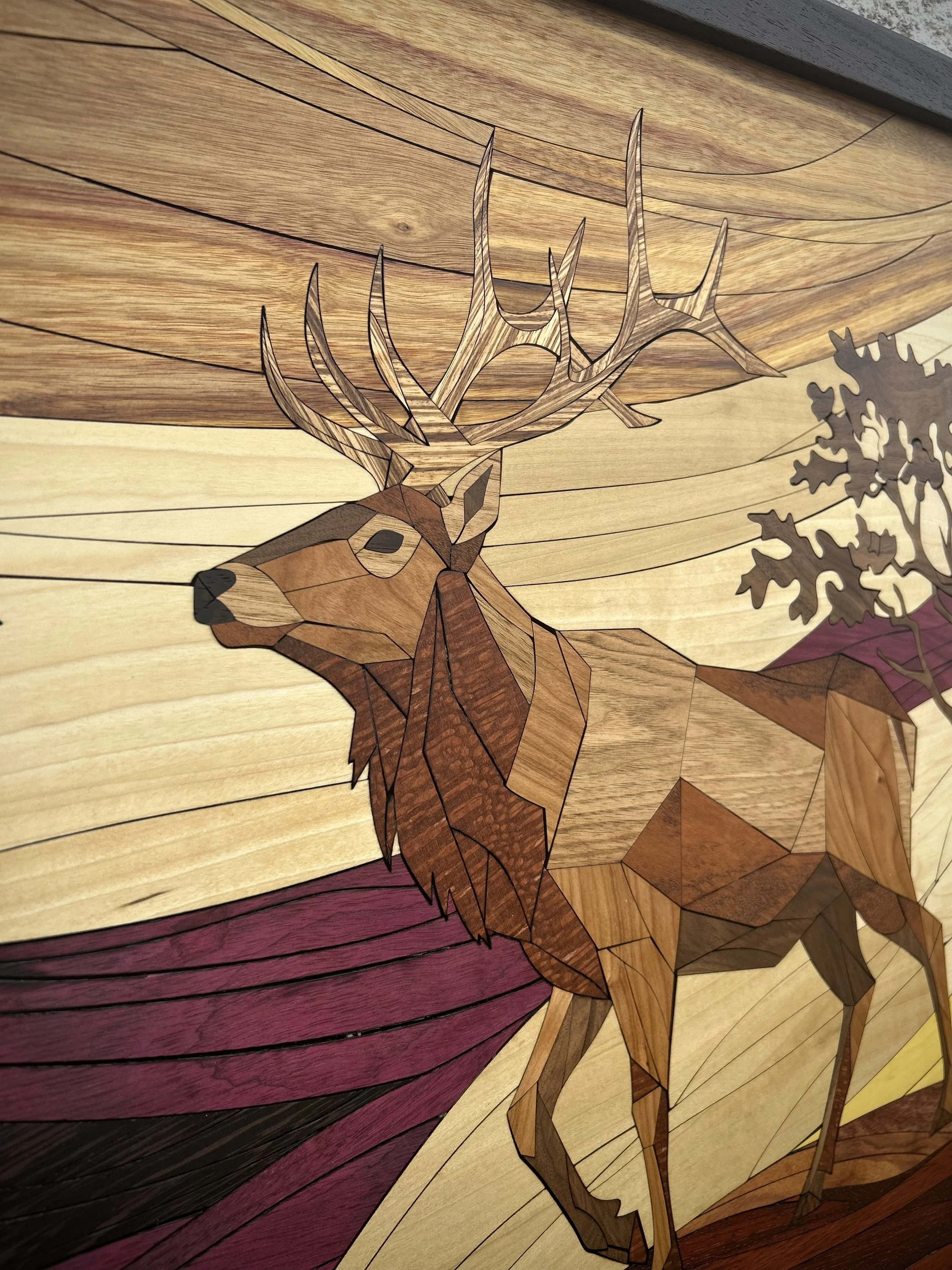 Wooden art piece depicting a buck with large antlers and a tree, using different wood tones and black lines for details.